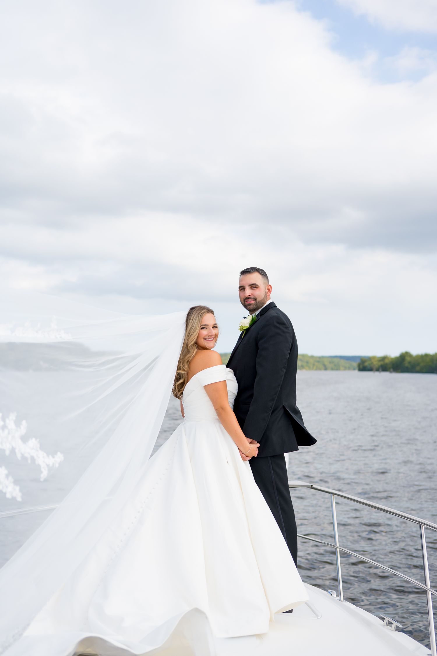 Romantic wedding photos captured on a boat with flowing veil against lake backdrop.