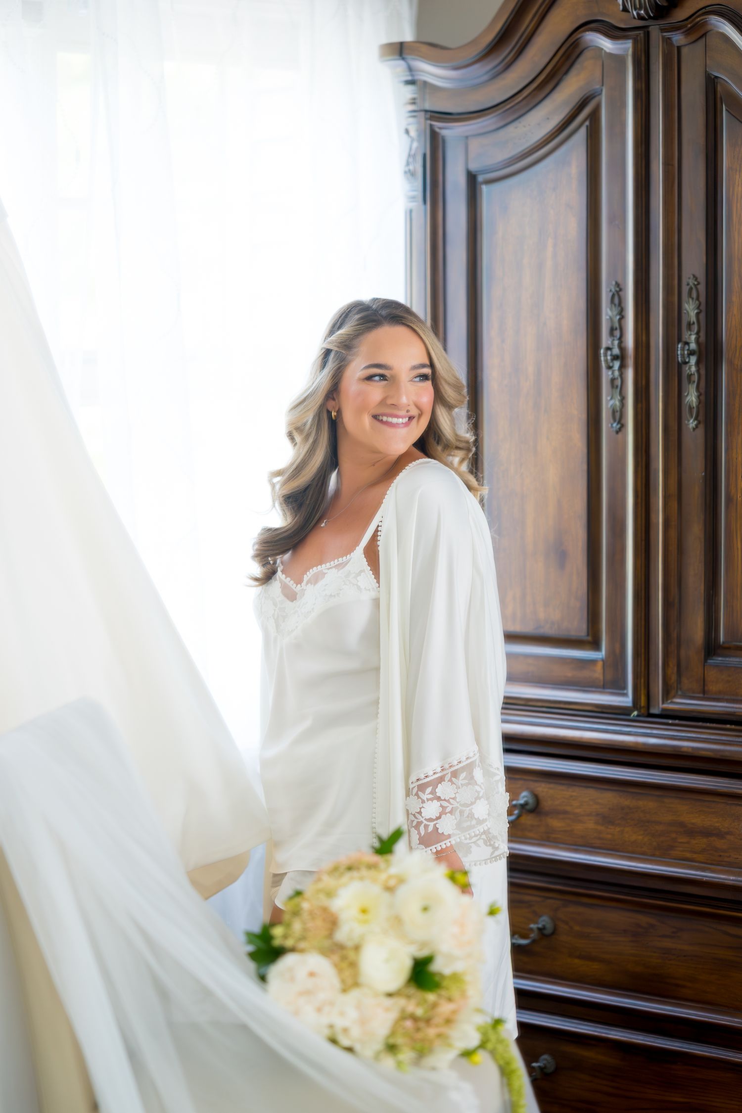 Wedding preparation scene with white dress and antique wooden armoire.