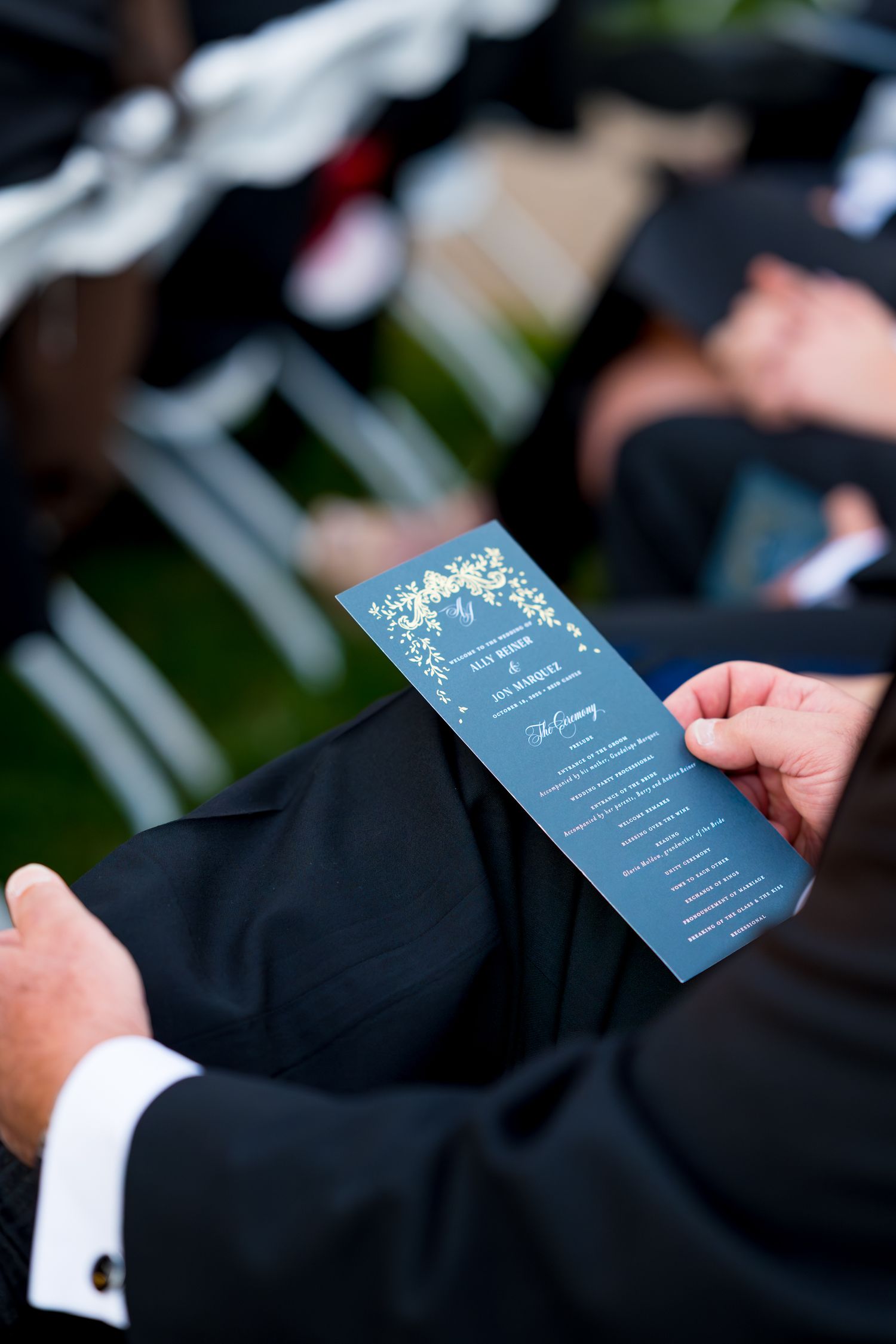 Hands holding a light blue wedding program or menu card against a dark background at an elegant event.