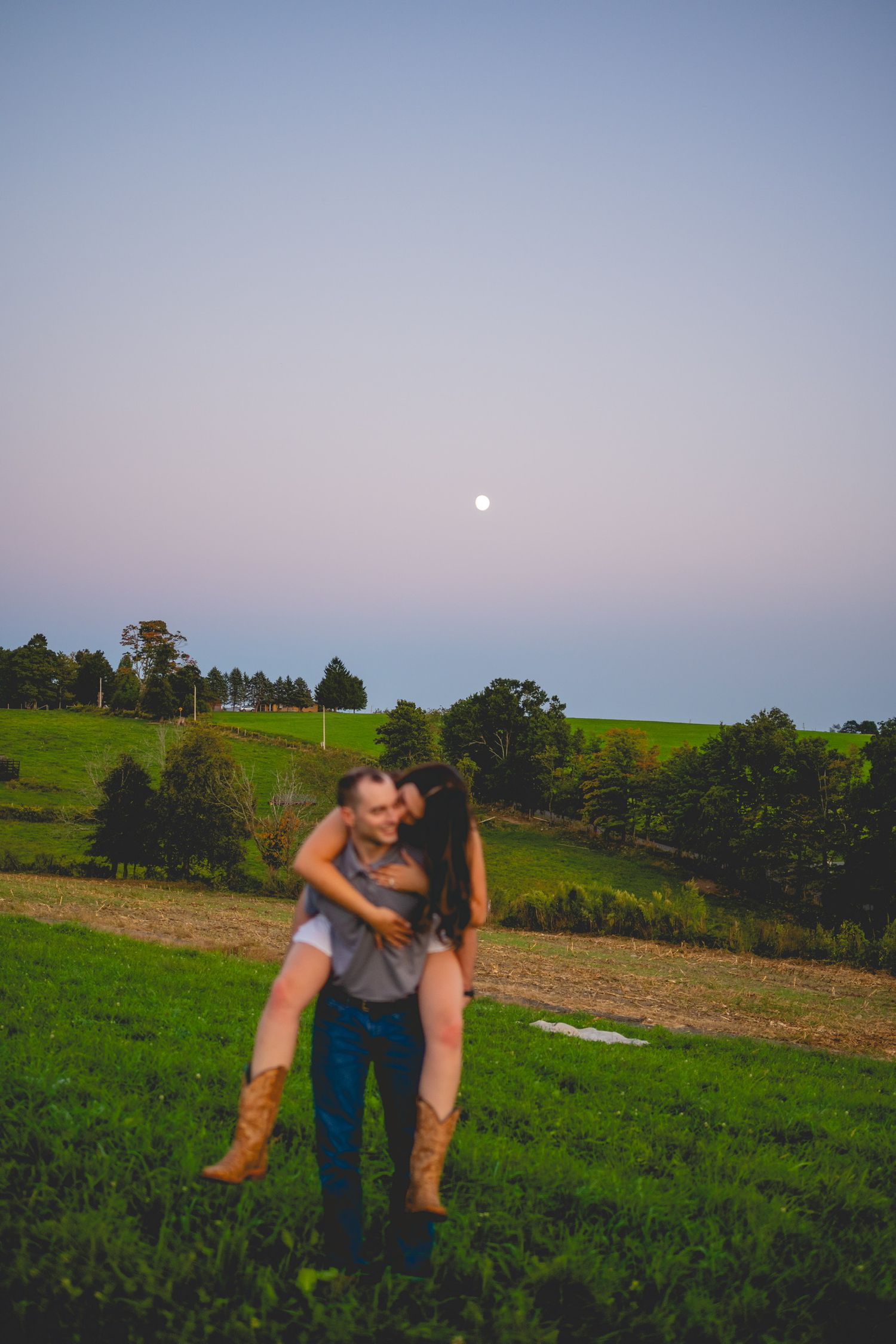 A romantic moment shared between two people in a green hillside field at twilight.