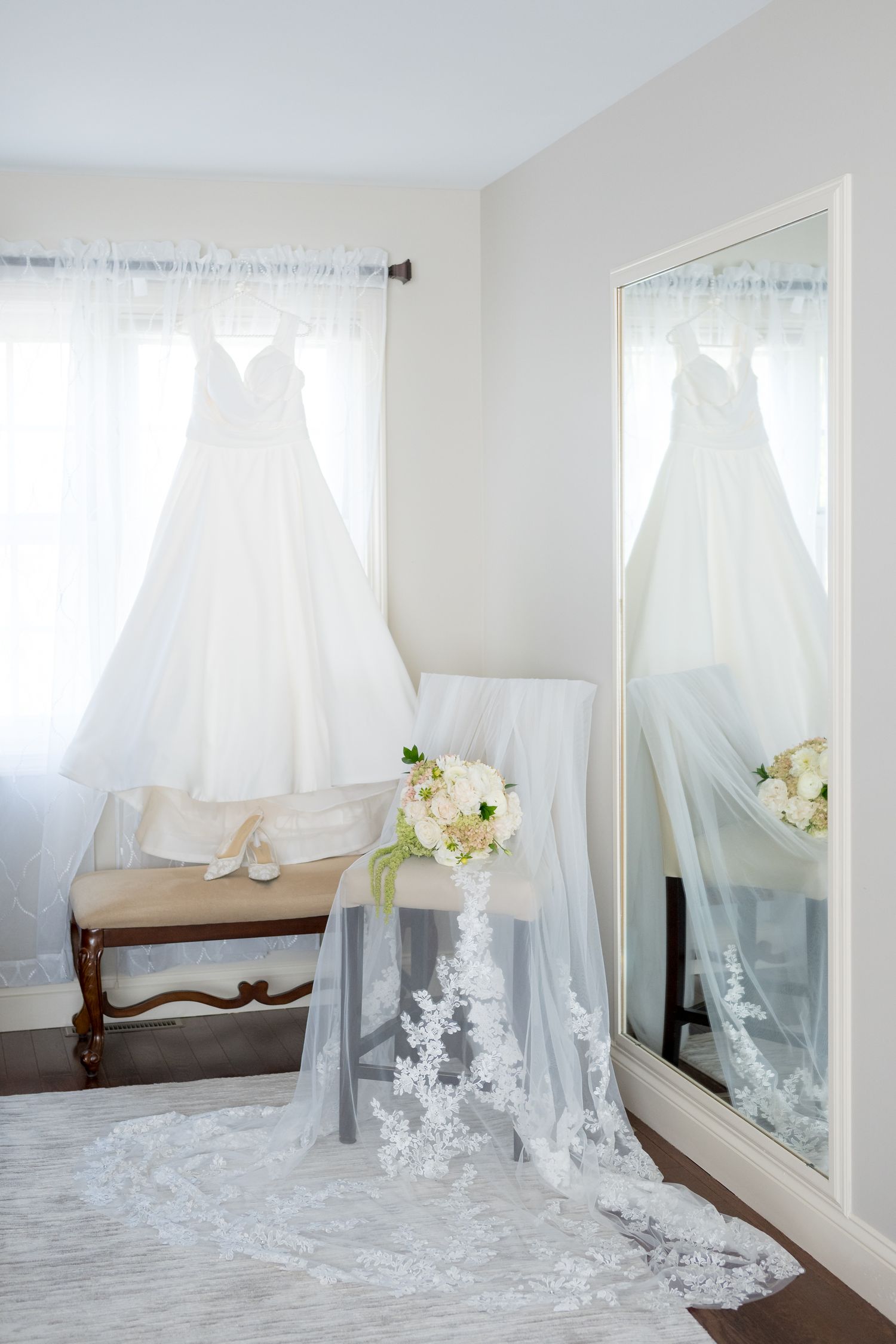A collection of white wedding dresses and veils displayed in a bright room with natural lighting and floral accents.