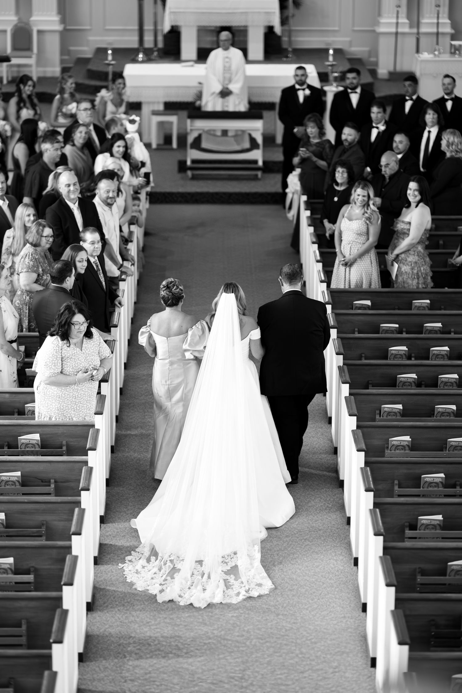 Traditional church wedding ceremony with guests seated in wooden pews decorated with white bows along the aisle.