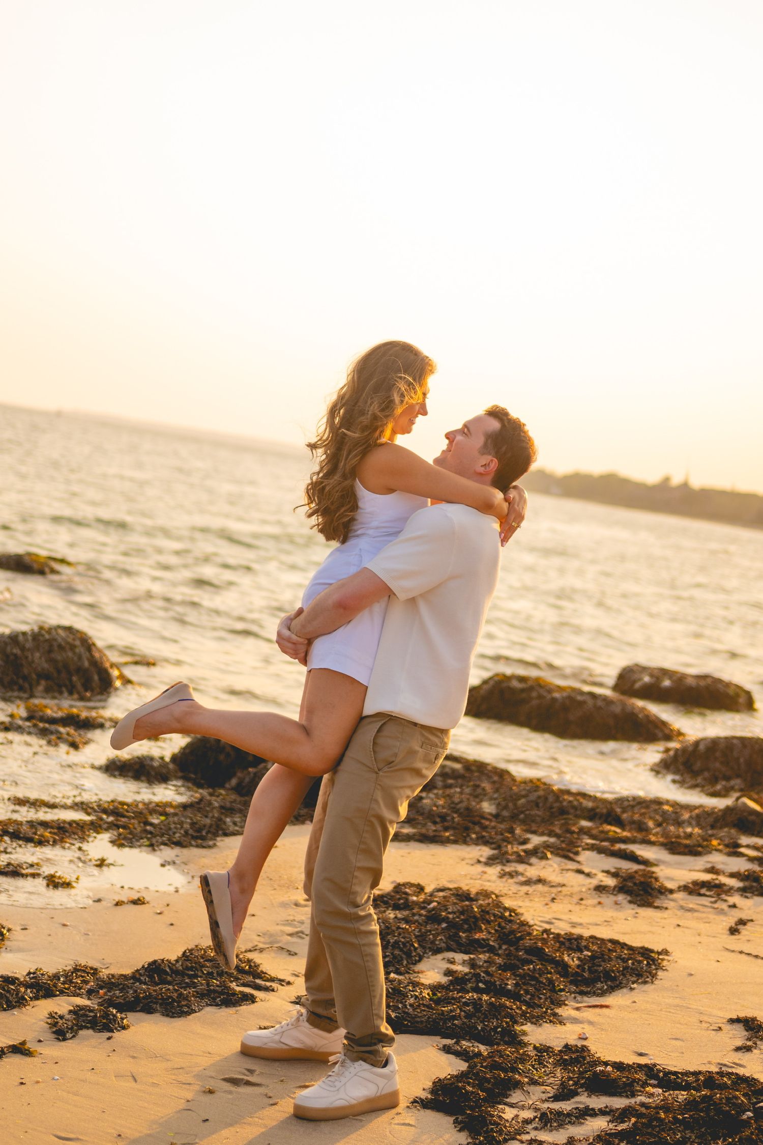 Couple embracing on sandy beach at sunset with ocean waves in background at Harkness Memorial State Park in Connecticut.