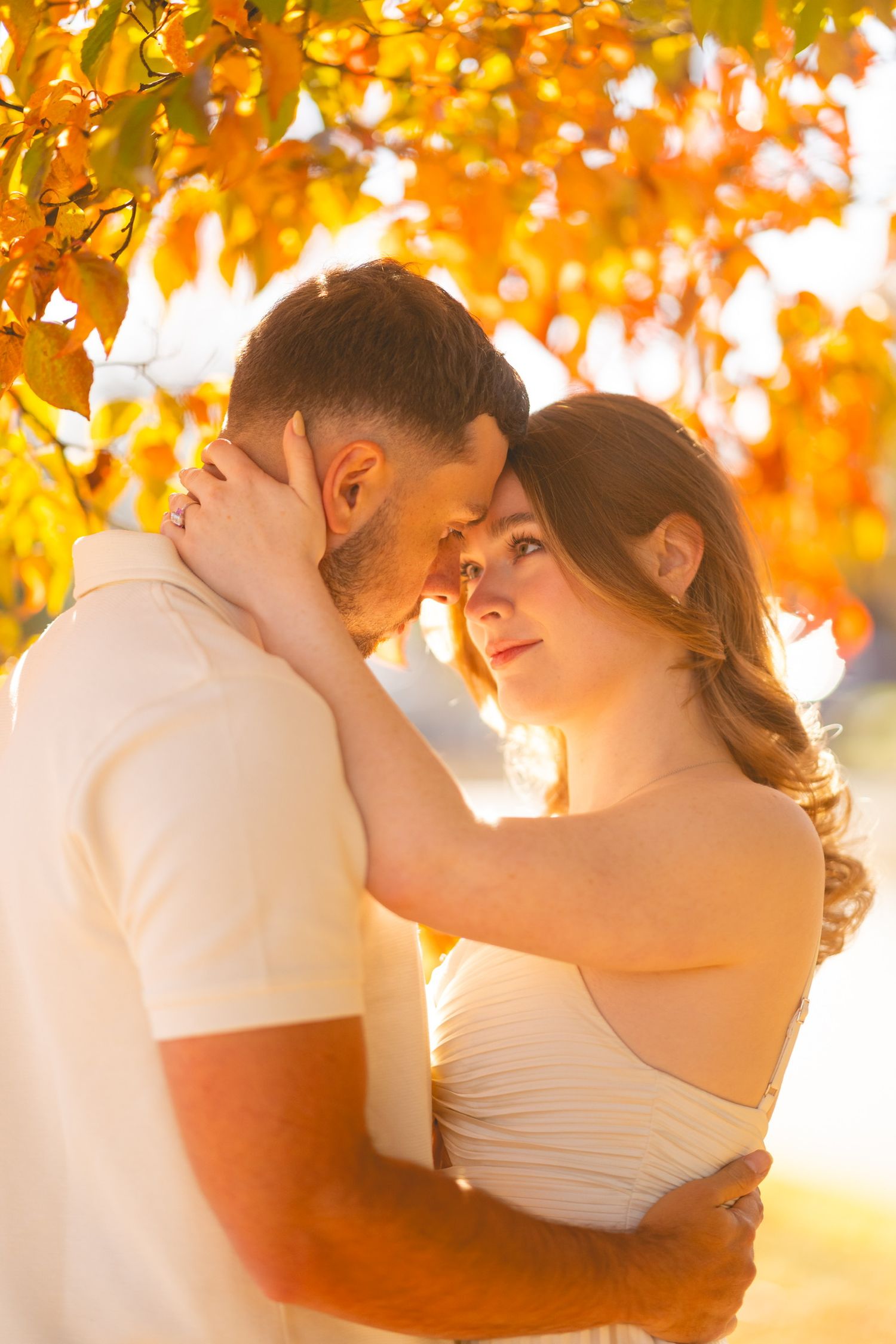 Romantic couple dancing under golden autumn leaves at sunset.