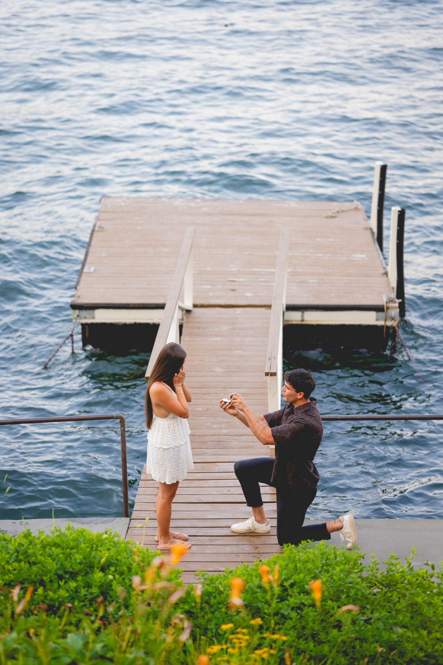 Marriage proposal moment on Candlewood Lake in Connecticut captured on a dock with orange flowers in foreground.
