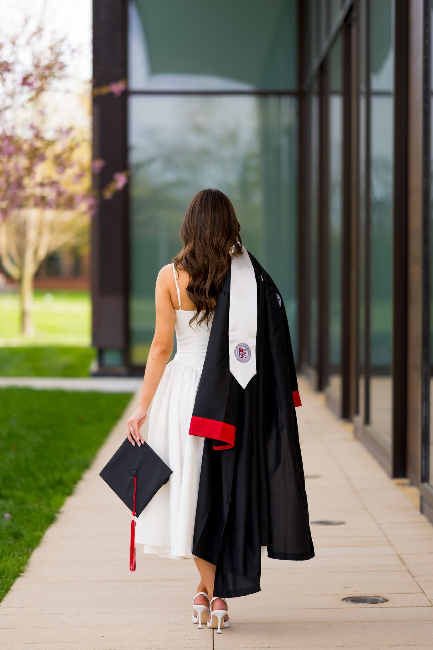 Sacred Heart University graduate walking along a modern building corridor in cap and gown.