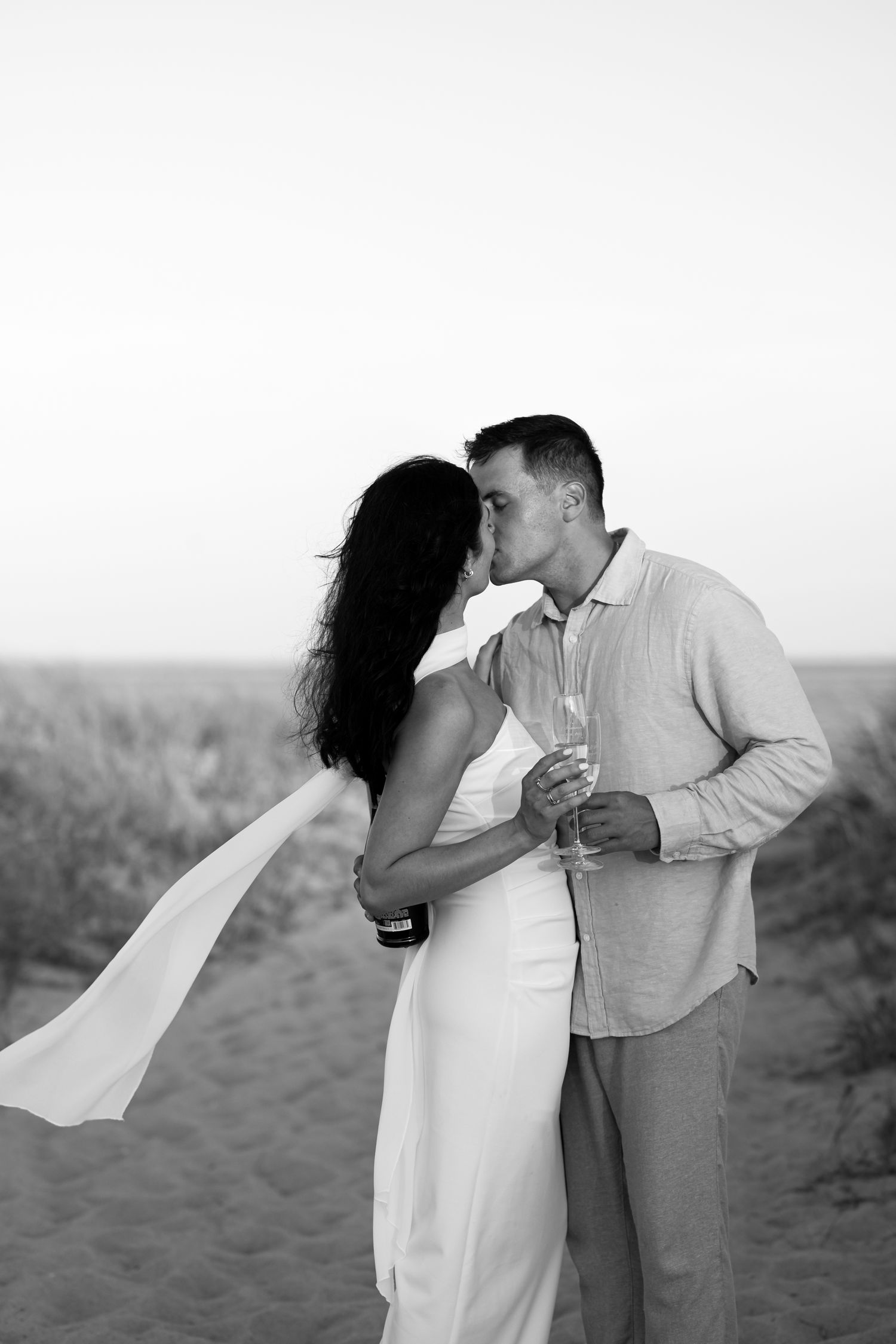Black and white photo of couple embracing on beach with flowing fabric at Chatham Lighthouse Beach in Chatham, Massachusetts.