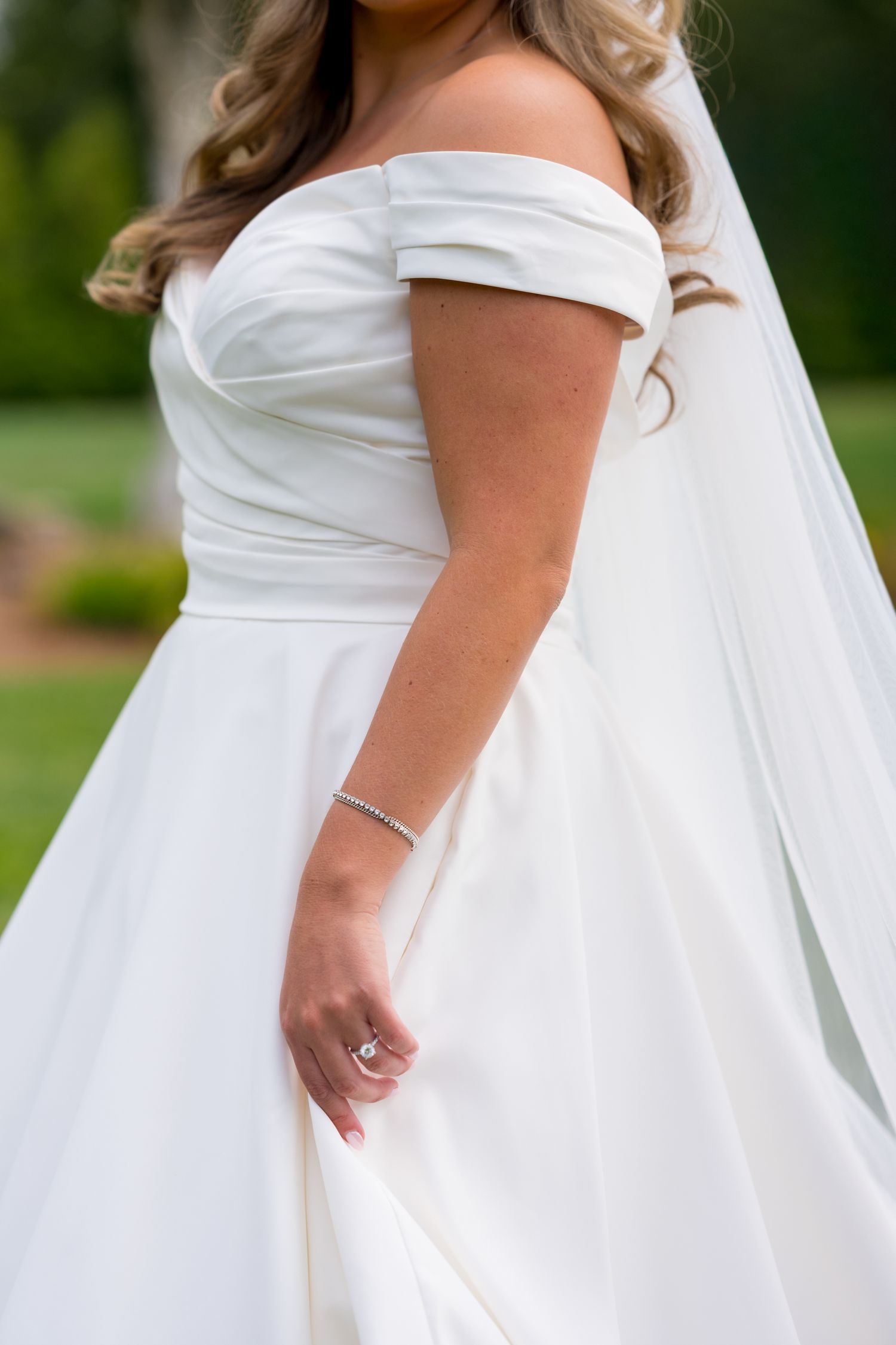 Close-up detail of off-shoulder white wedding dress with pleated bodice.