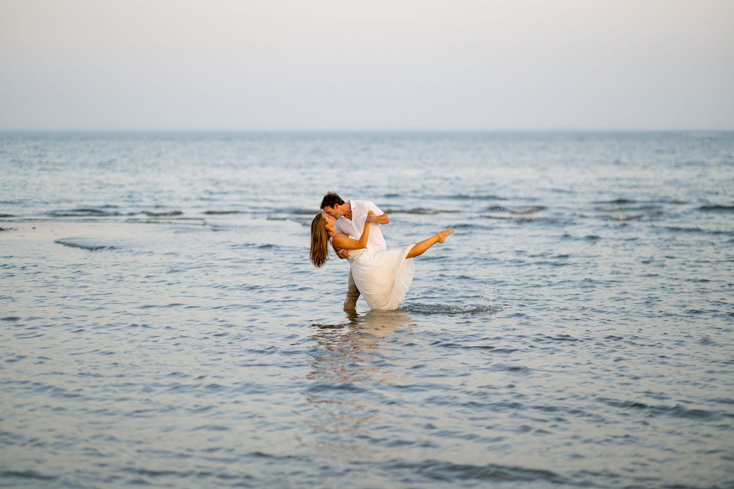 A series of photos showing a person in a white dress twirling and dancing in shallow ocean waves at sunset.
