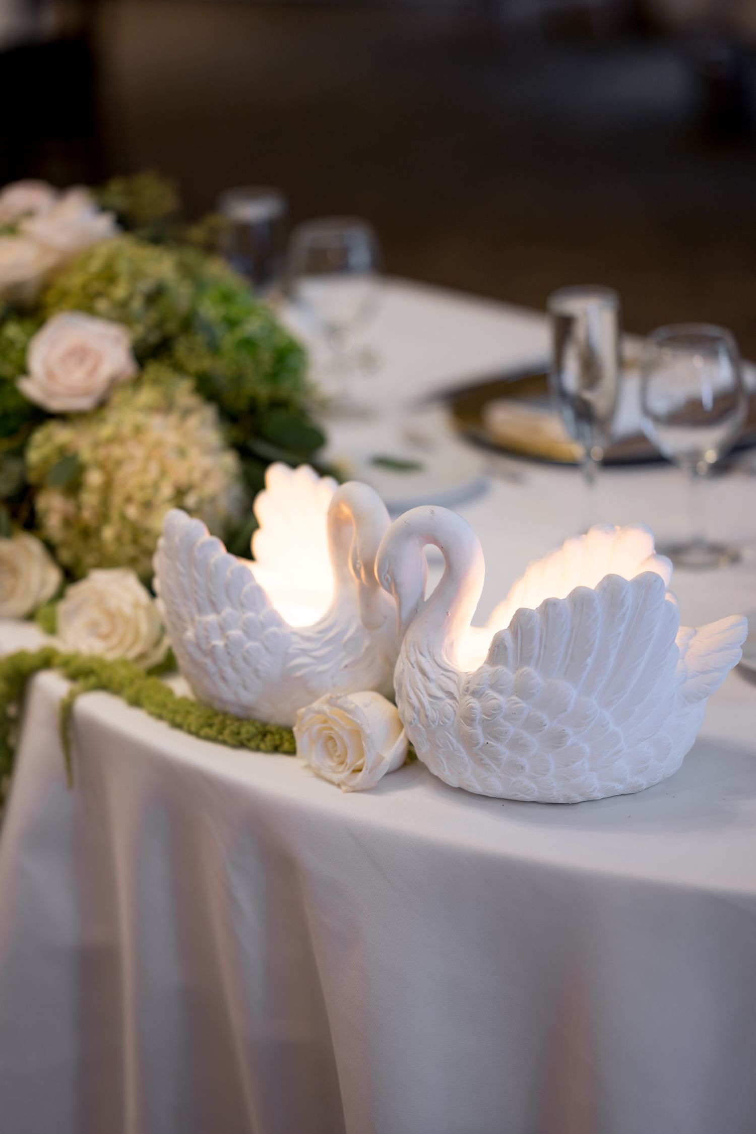 White ceramic swan candle holders and roses create an elegant table centerpiece.
