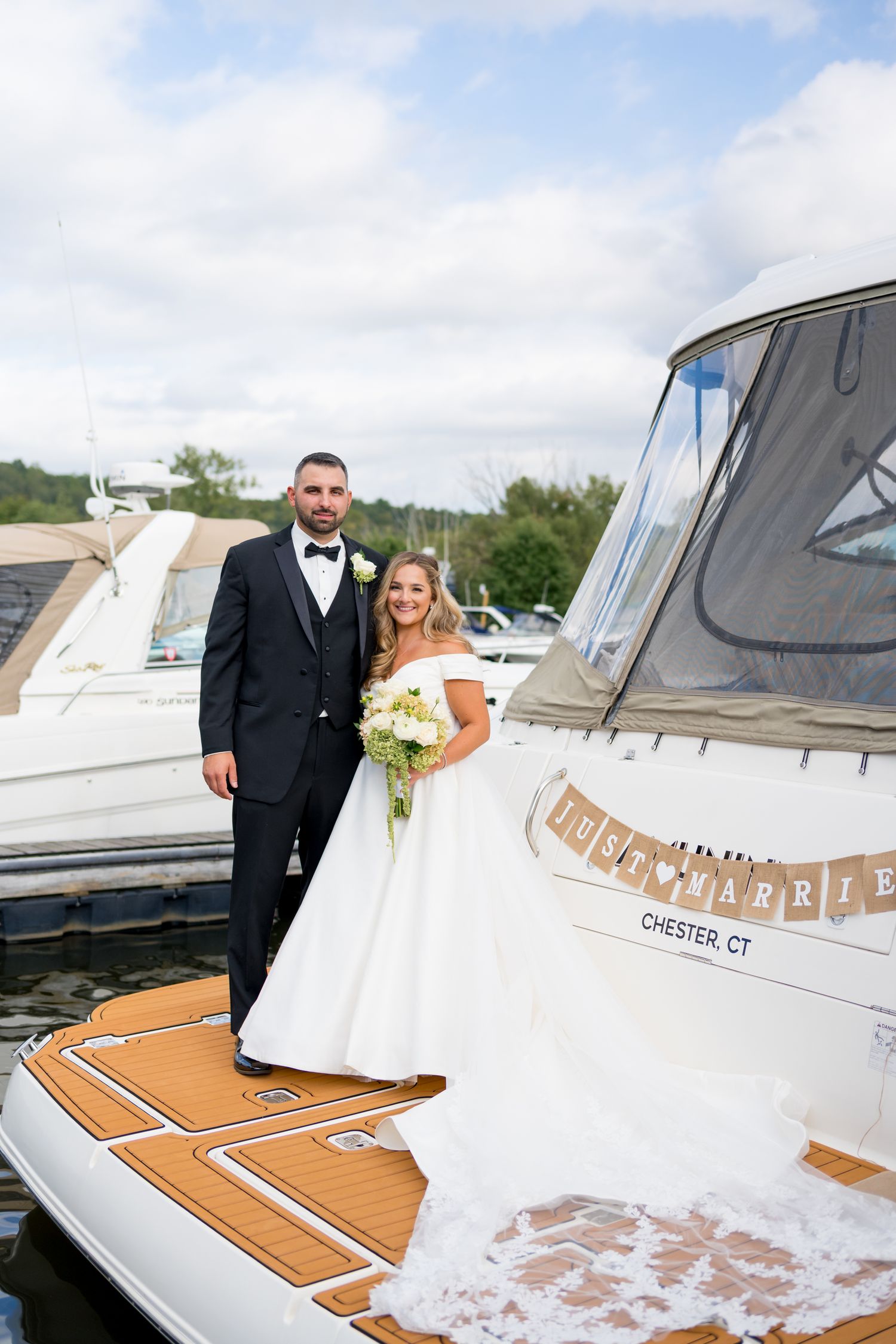 Wedding couple posing on a luxury yacht deck with wooden details and white upholstery.