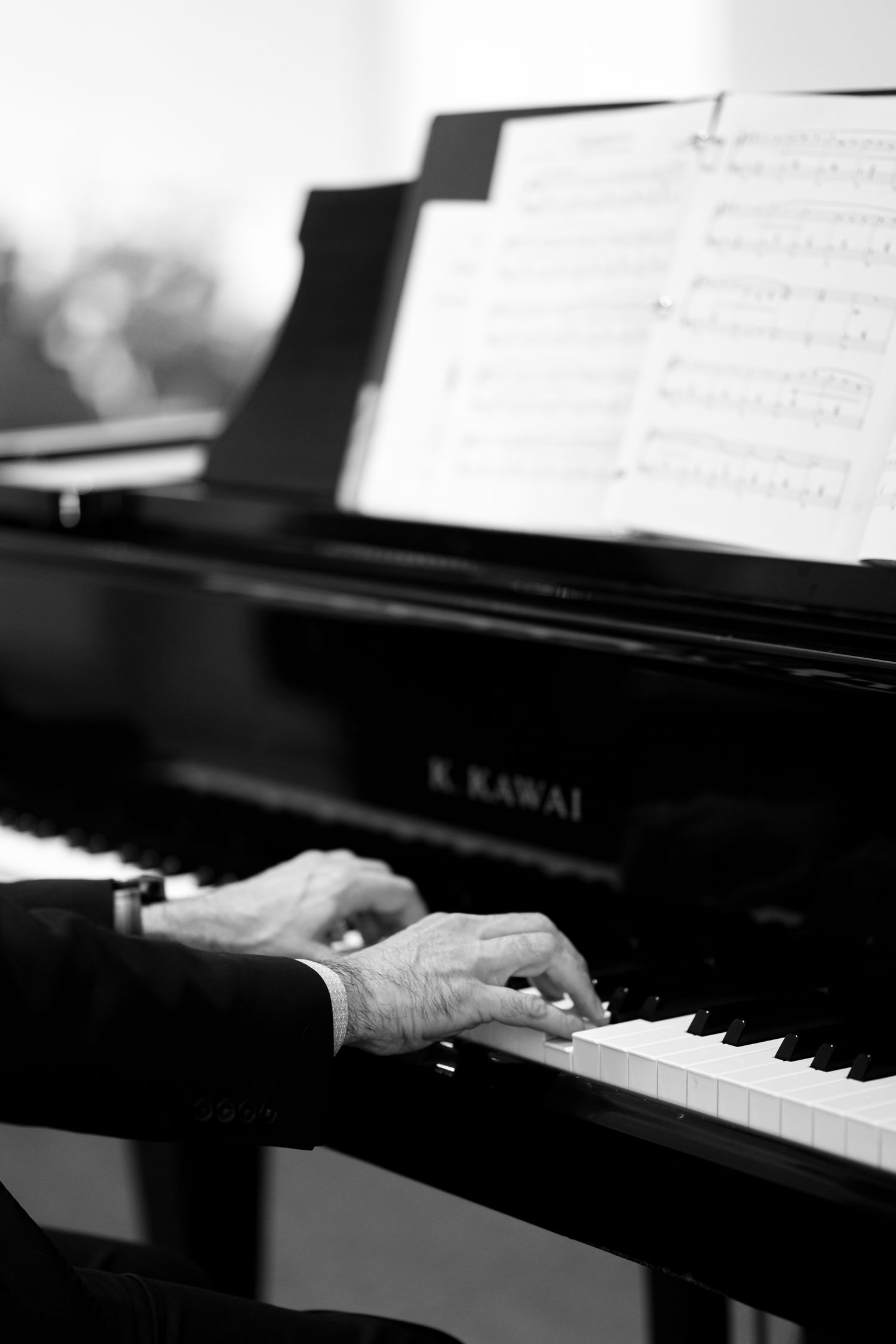 Hands playing a black Kawai piano keyboard in dramatic black and white lighting.