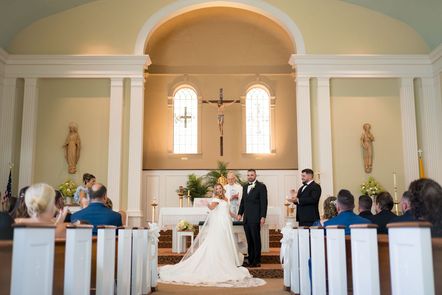 A panoramic view of a traditional church wedding ceremony with white pews and stained glass windows.