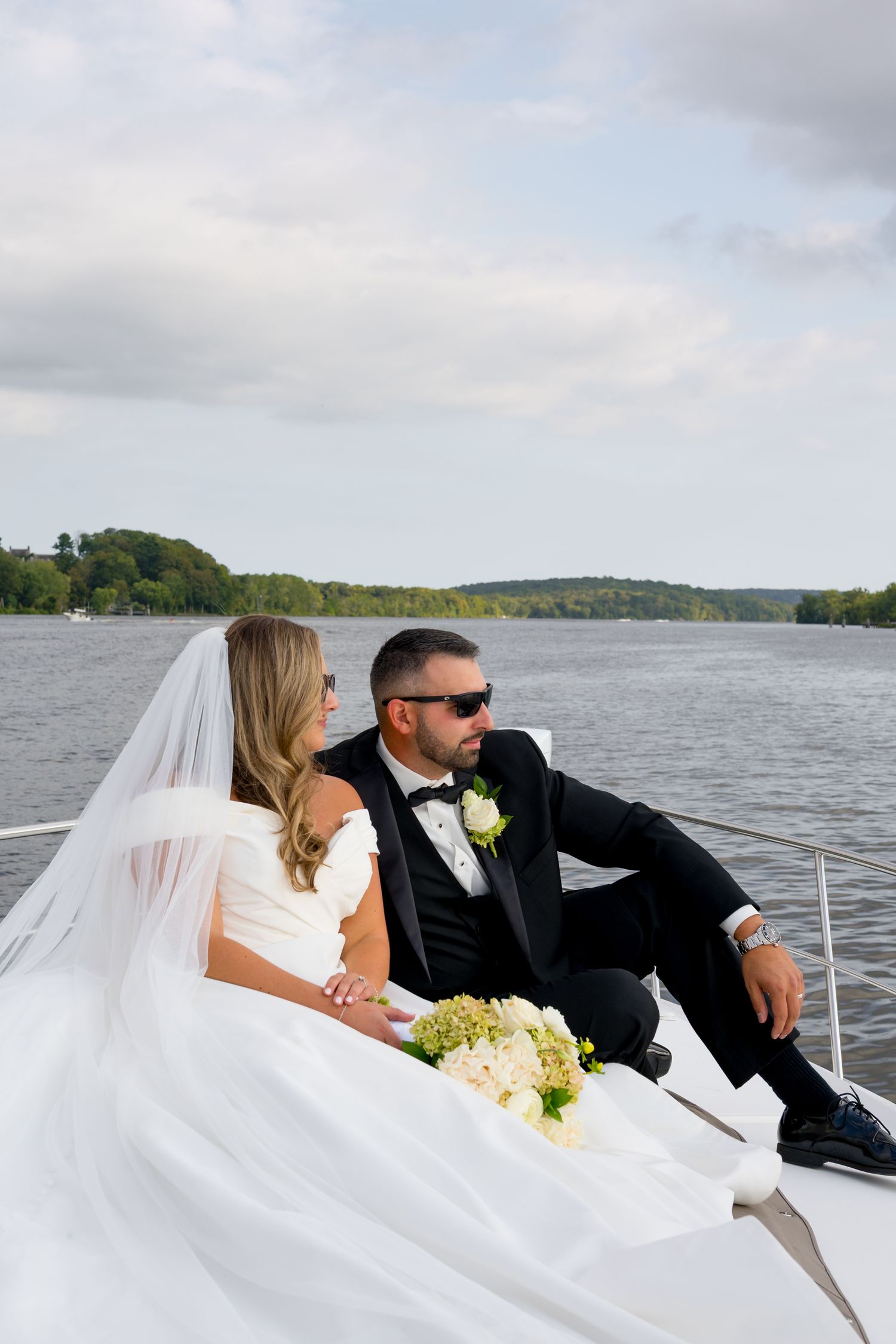 Newlyweds relaxing on boat deck with waterfront backdrop.