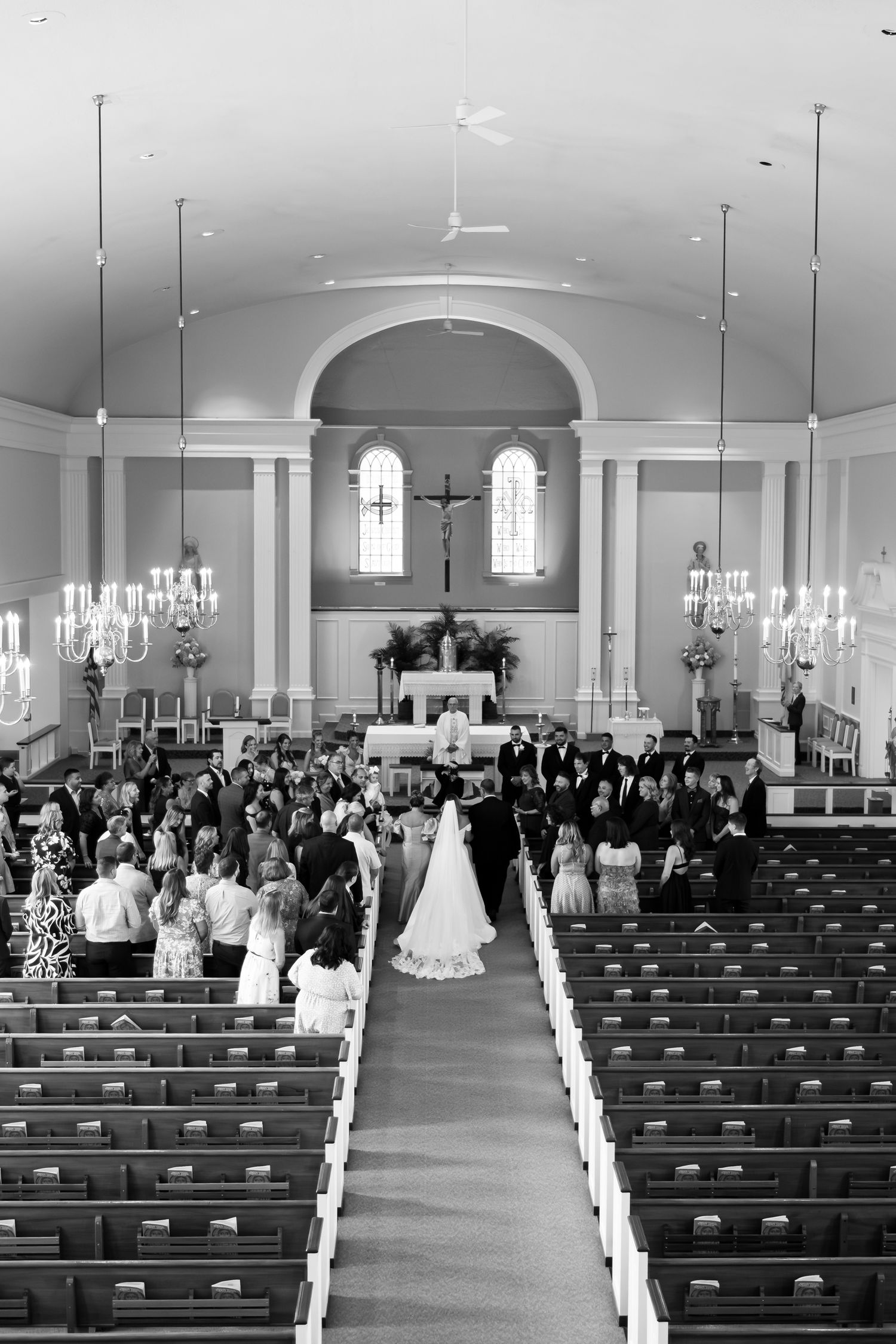 Black and white view of traditional church wedding ceremony with guests seated in wooden pews.