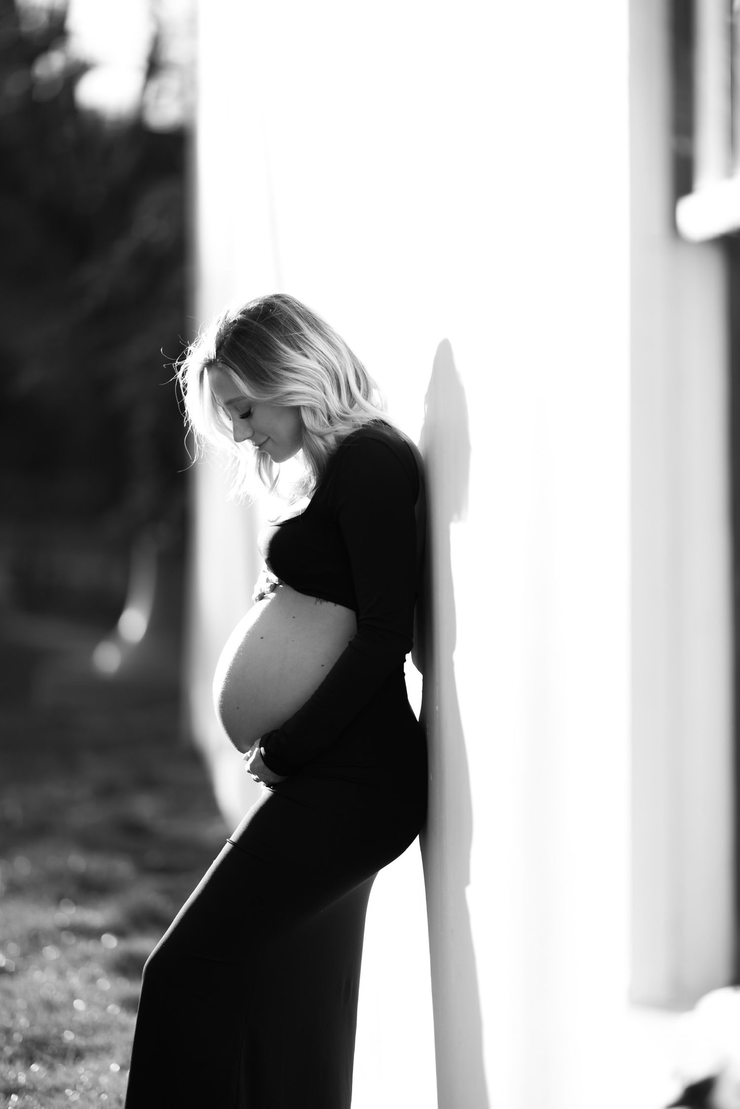 Silhouette maternity photos against white wall in dramatic lighting.