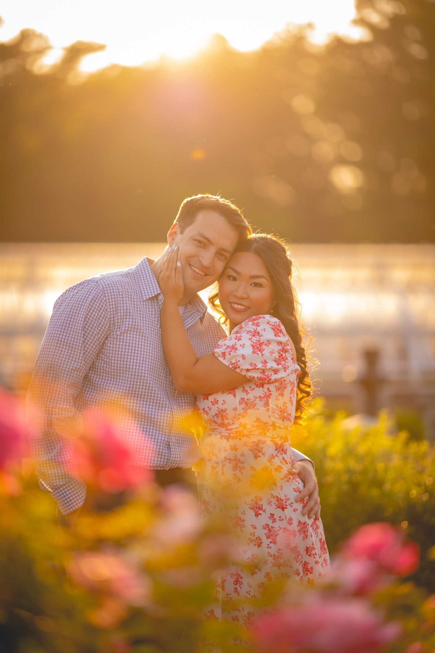A couple shares a tender moment in a garden with pink flowers during golden hour.