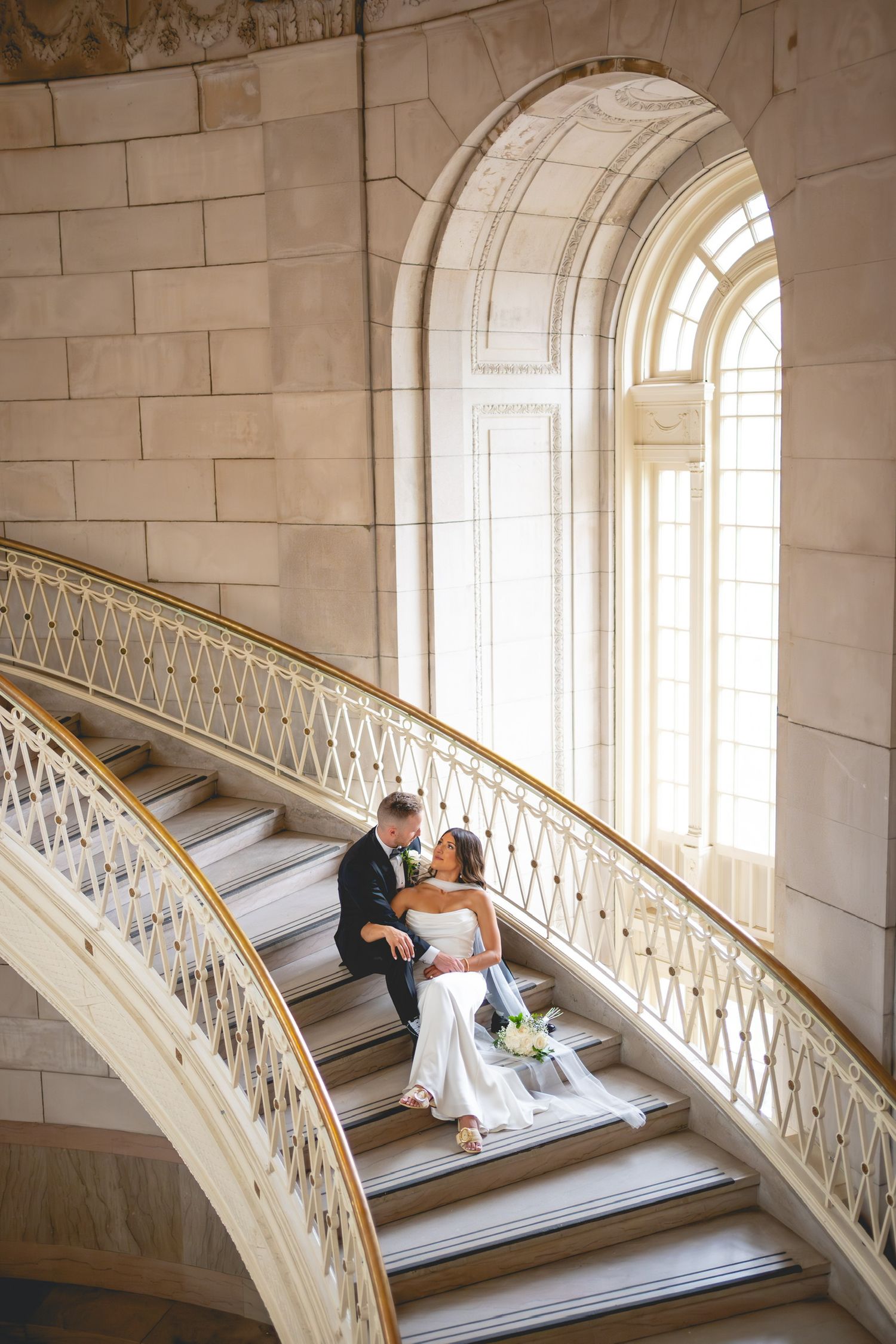 Bride and groom share intimate moments on ornate marble staircase with arched windows at Hartford City Hall in Connecticut.