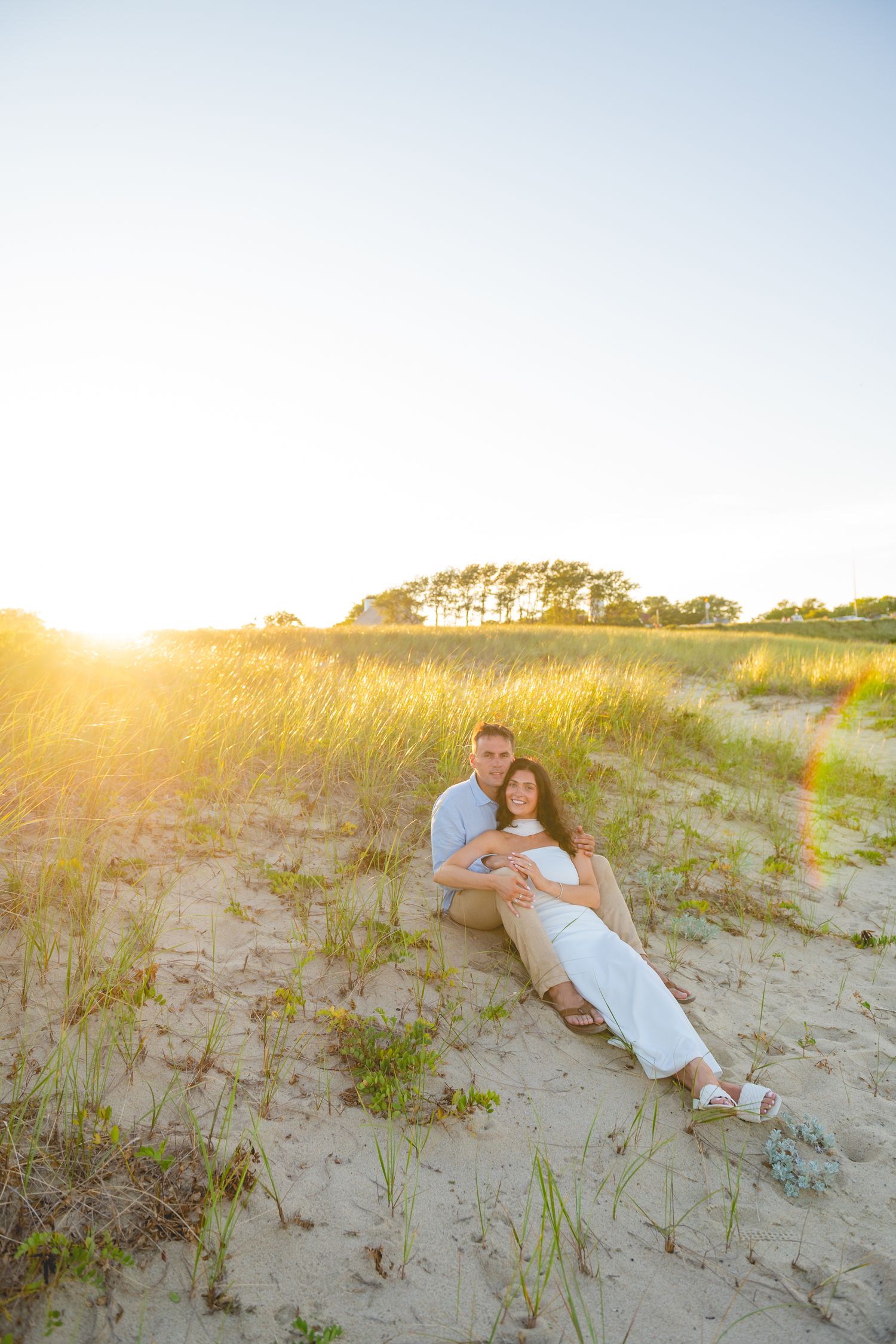 A couple relaxing on sandy dunes at Chatham Lighthouse Beach in Chatham, Massachusetts during golden hour sunset.