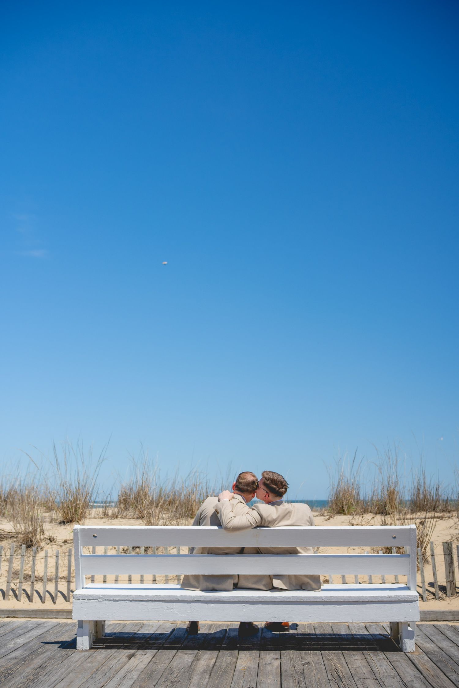 A wooden boardwalk stretches along a sandy beach under bright blue skies.
