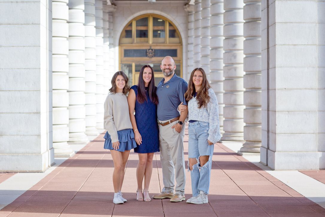 Group portrait of five people standing under white columned archway.