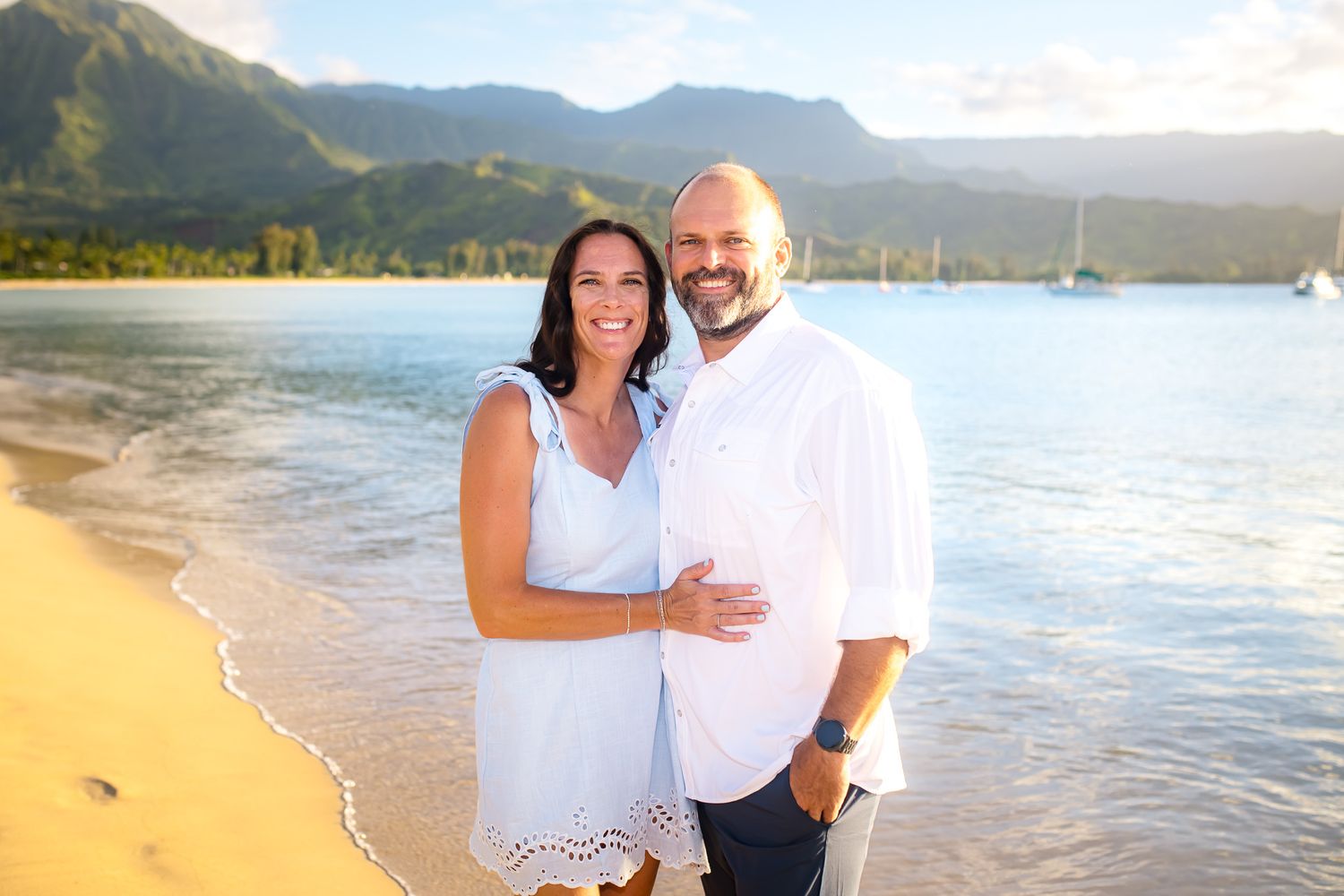 Sunset beach scene with mountains and couple in white attire.