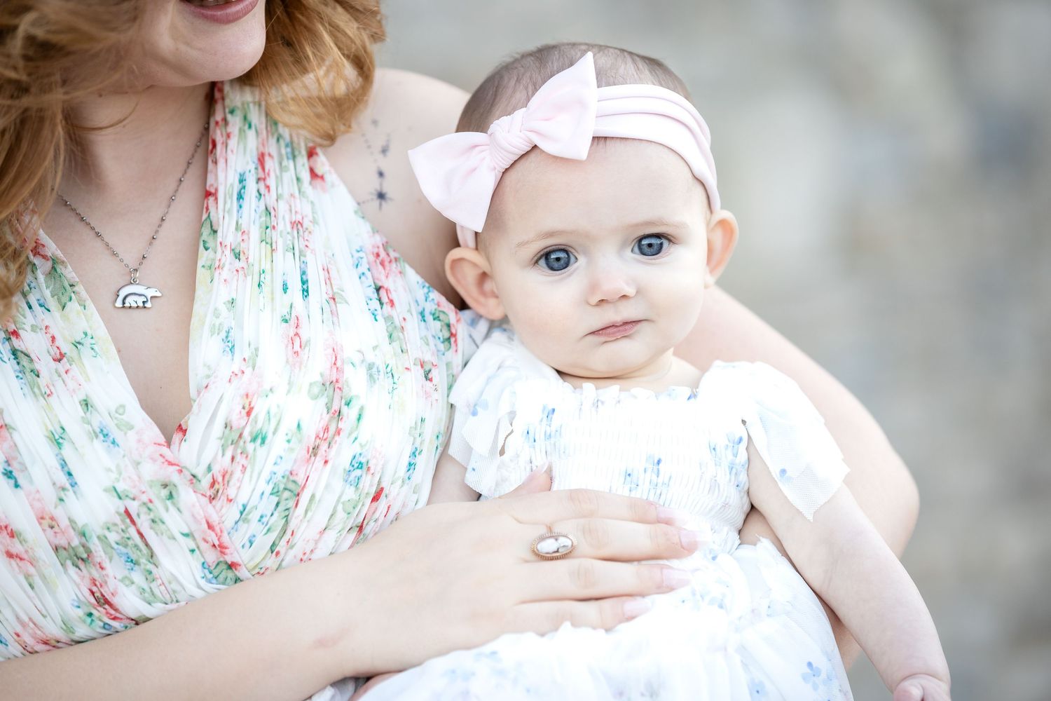 Baby in white dress and bow photographed against neutral background in studio setting.