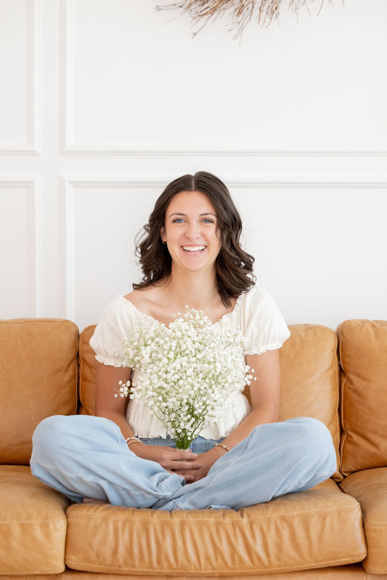 Someone sits cross-legged on leather couch holding fresh baby's breath flowers in casual attire.
