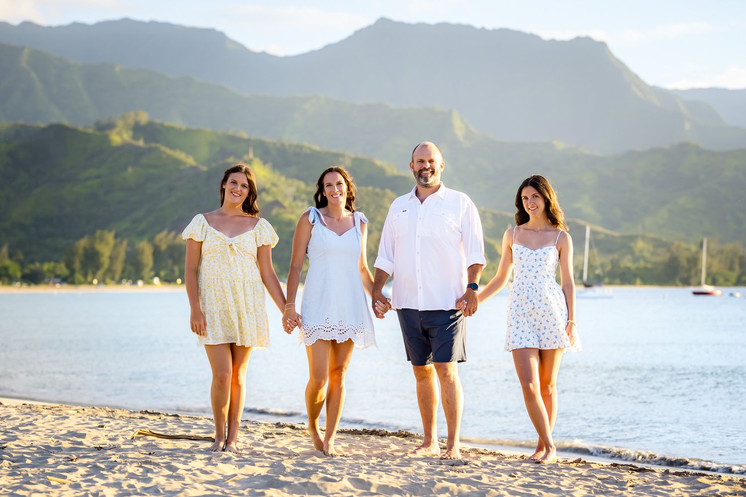 Family group walking along beach shoreline with mountain backdrop in Hawaii.