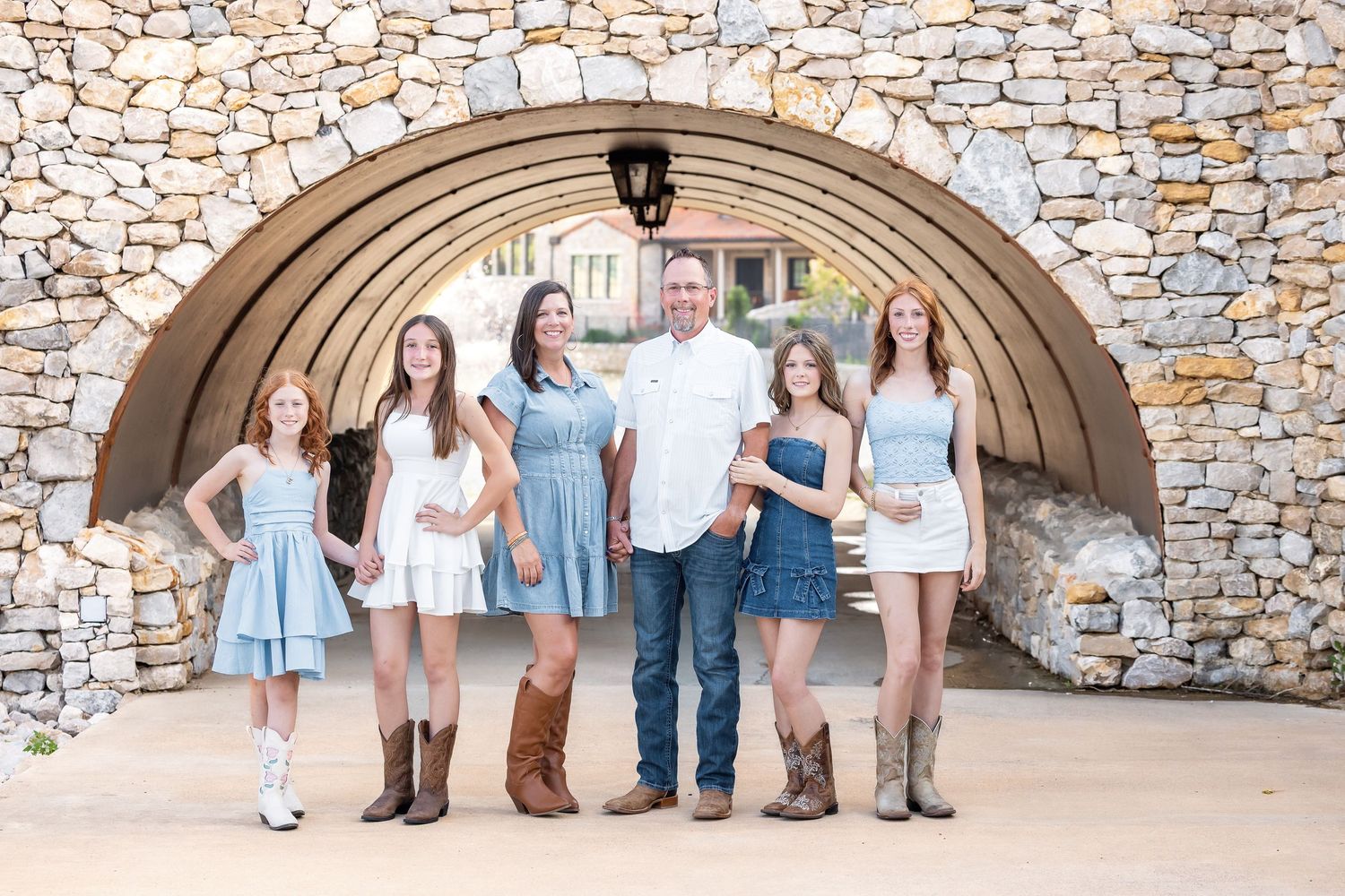 A family of five poses under a stone arch, wearing coordinated blue and white outfits with cowboy boots.