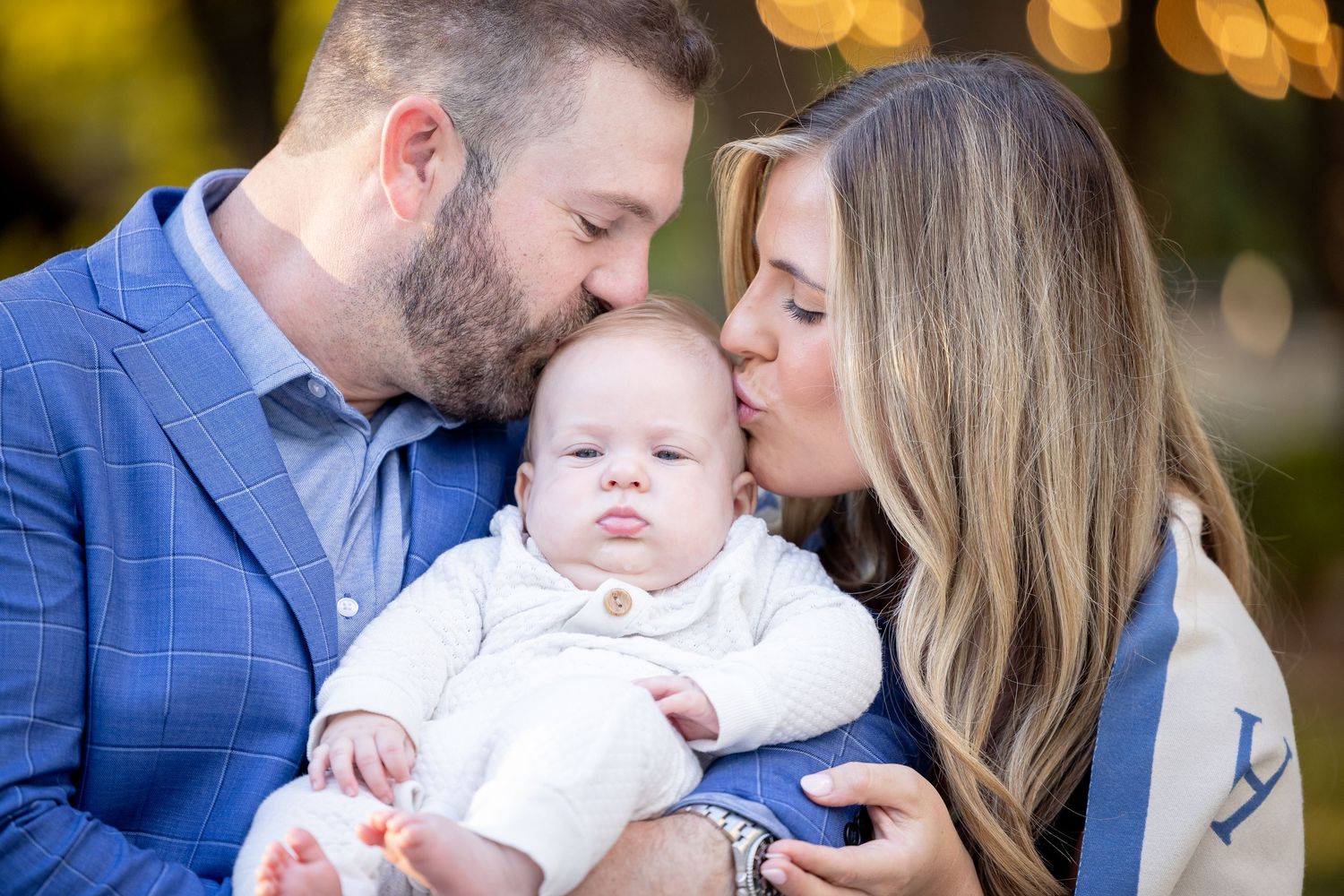Intimate family portrait with parents and baby outdoors with warm bokeh lighting effect.