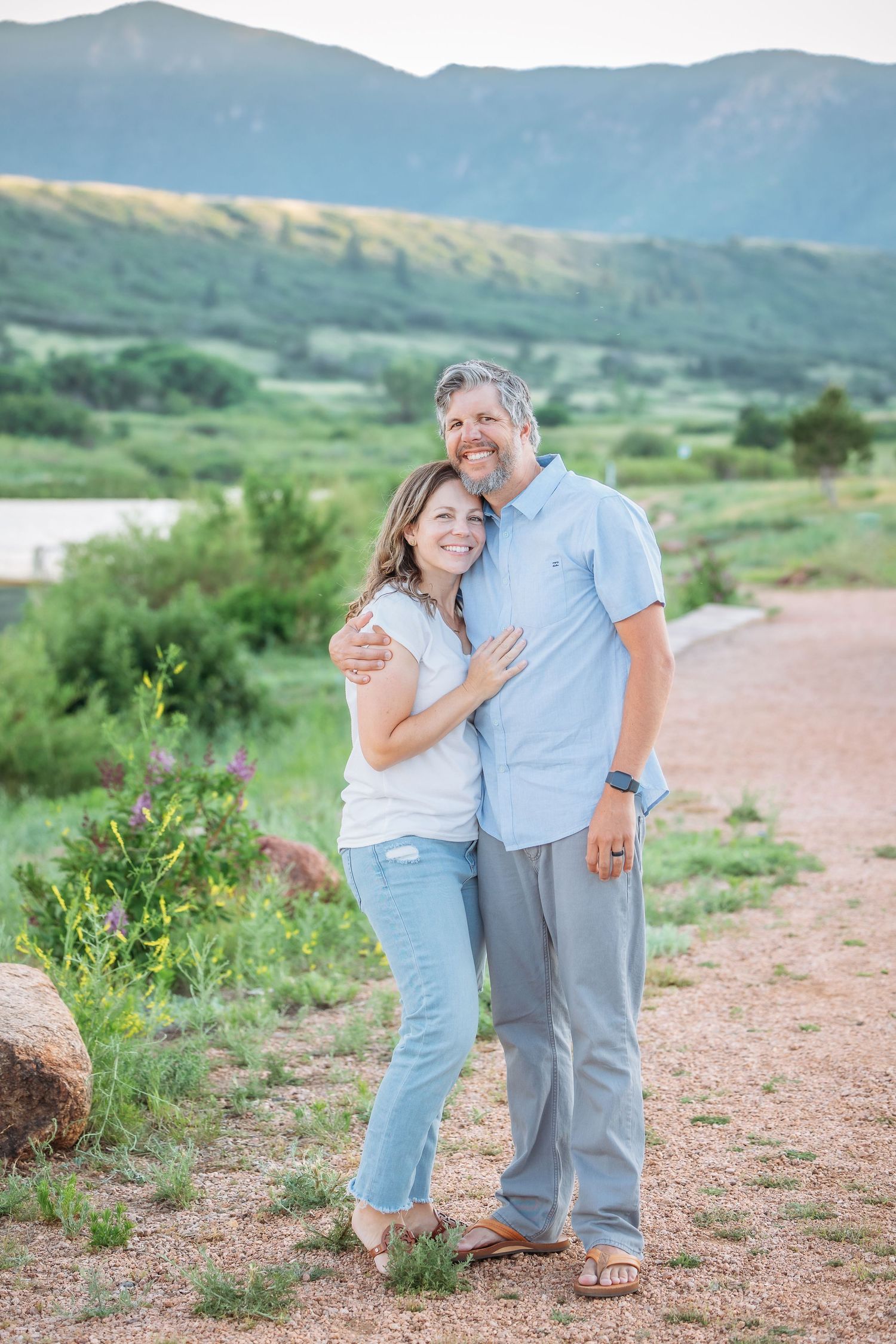 Couple embracing on a hiking trail with mountain views in the background.