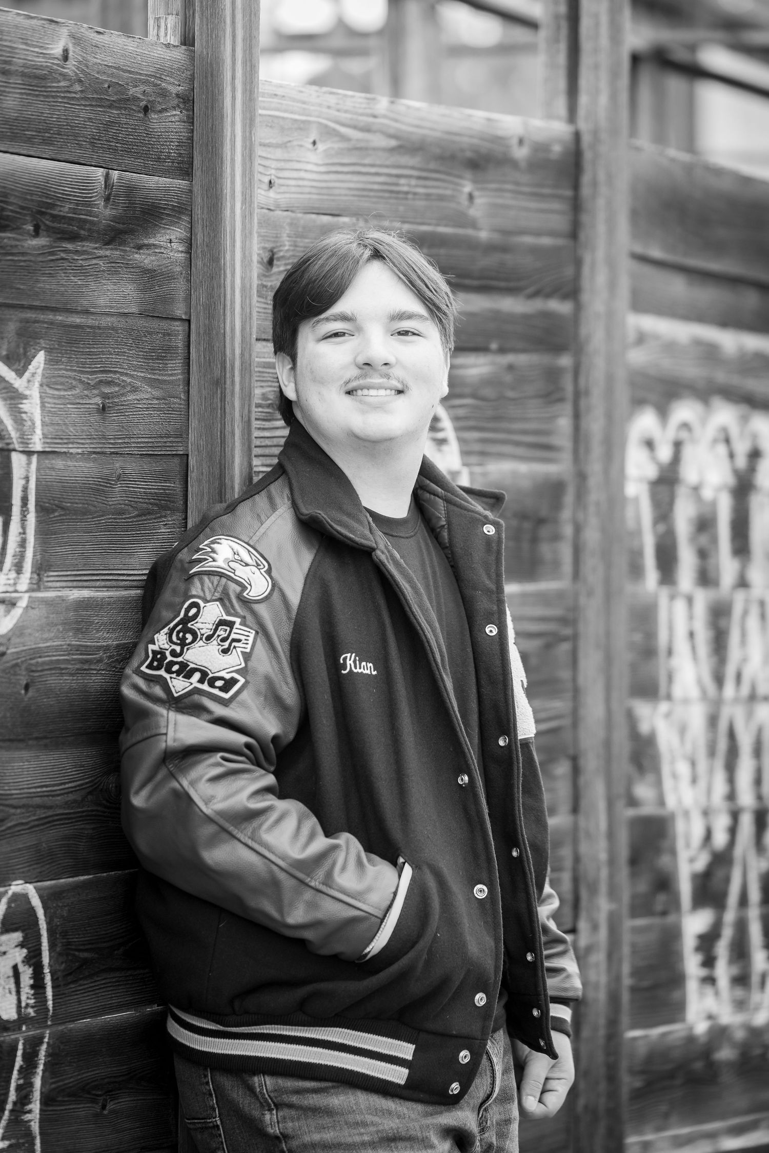 Portrait session against rustic wooden wall with varsity jacket styling.