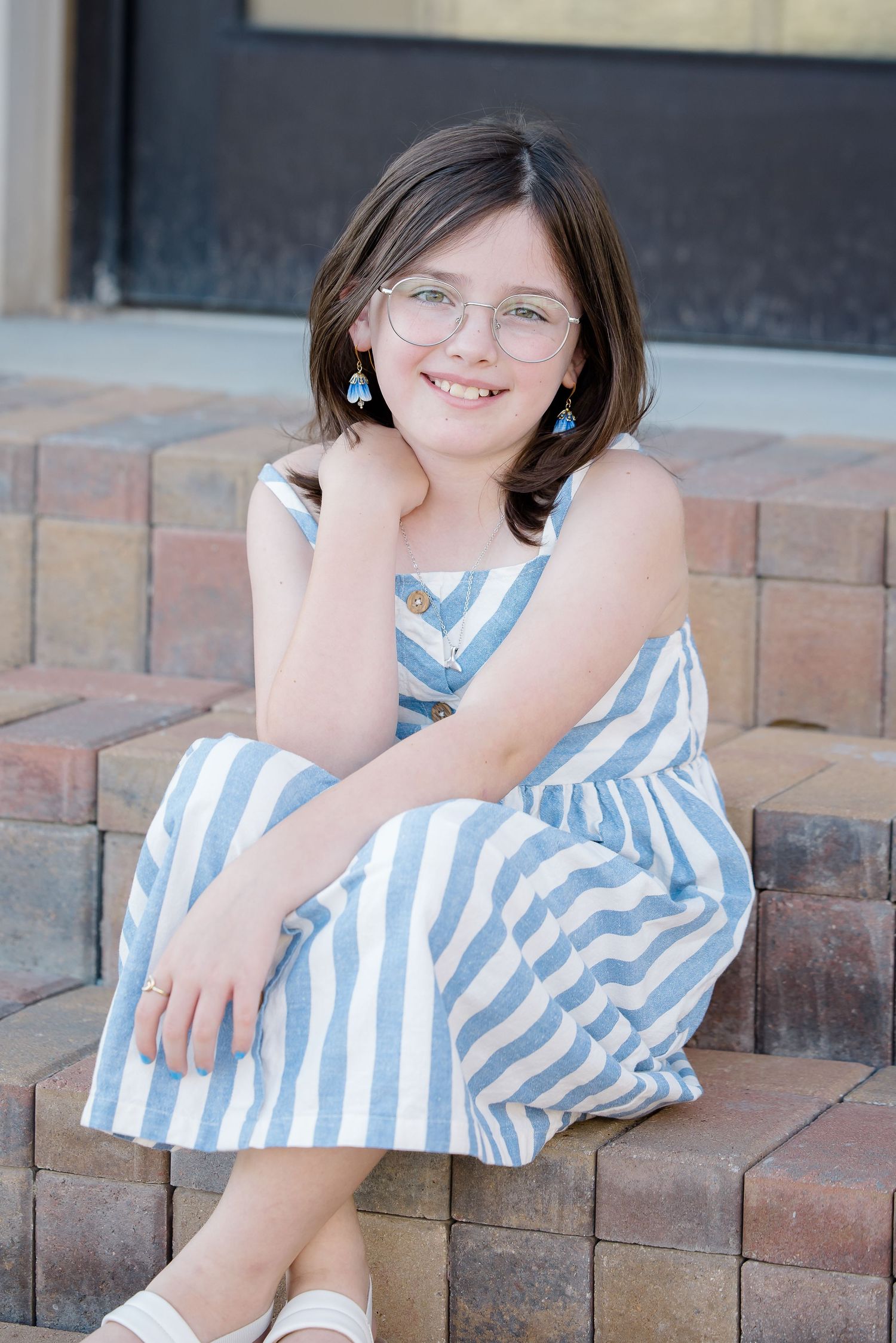 A portrait of someone in a blue and white striped dress sitting on brick steps.