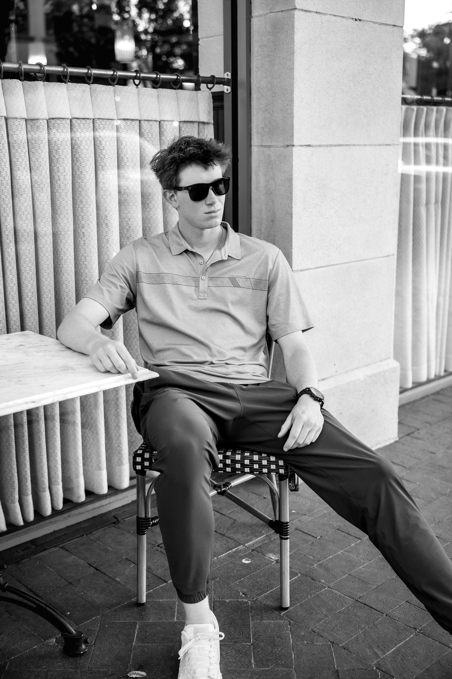 Black and white photo of person relaxing in casual attire on a porch with railings.