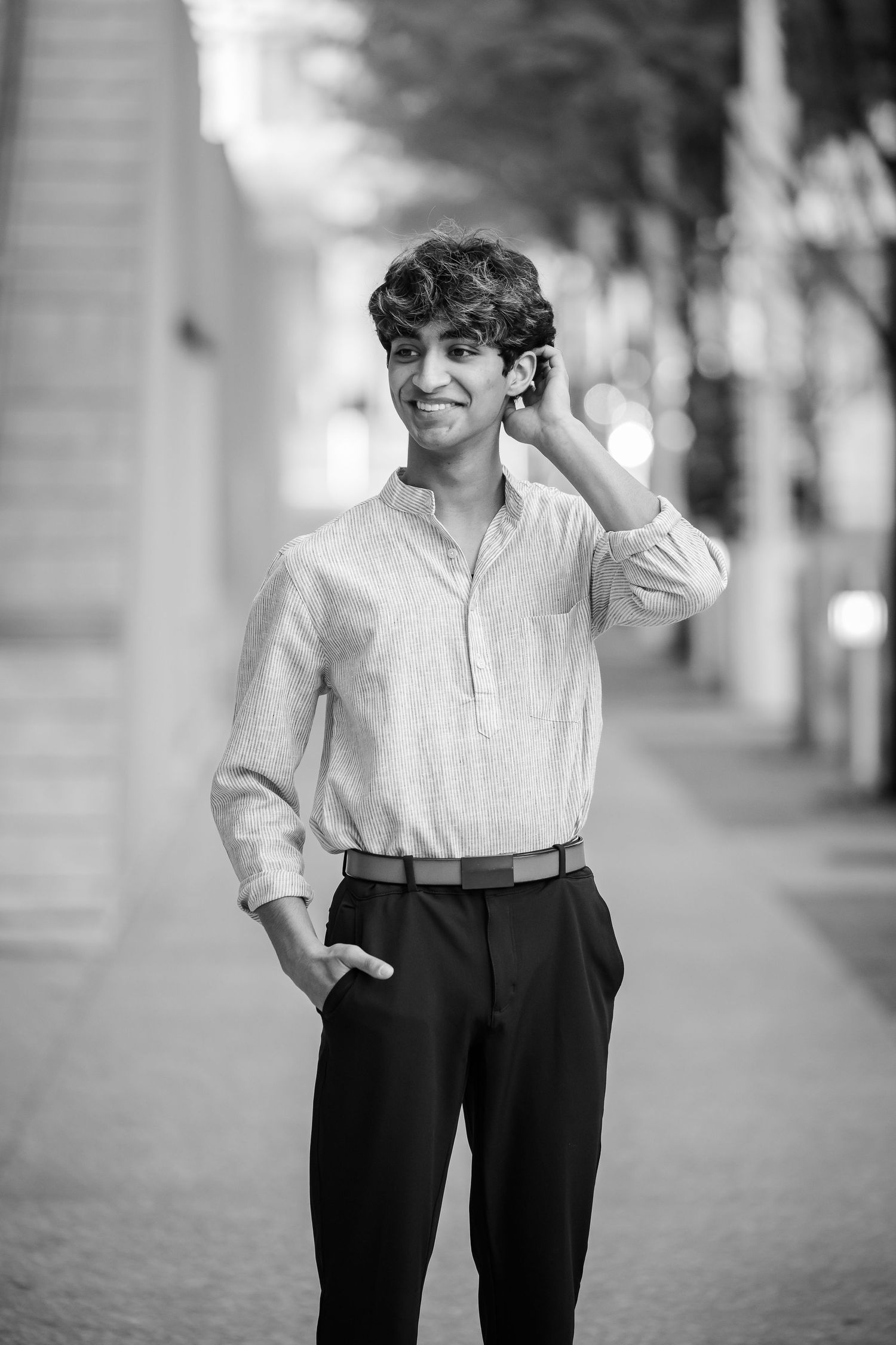 Black and white portrait of a young man with curly hair in a linen shirt and dress pants, smiling outdoors.