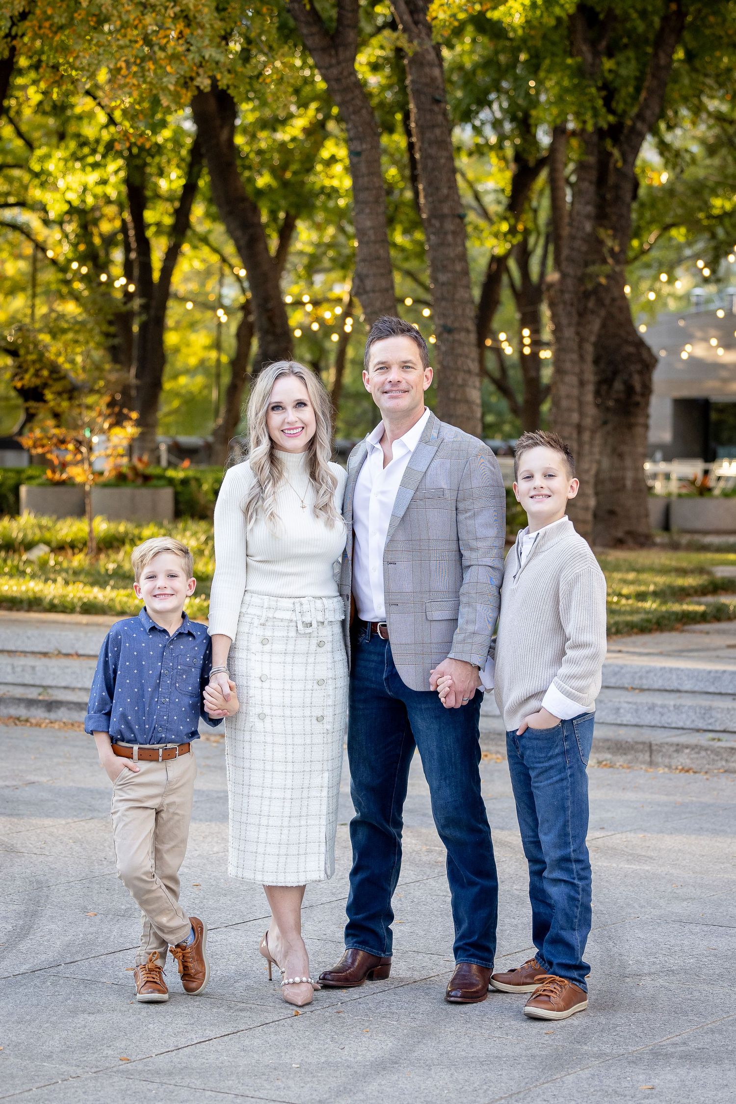Well-dressed family of four posing outdoors among fall trees.