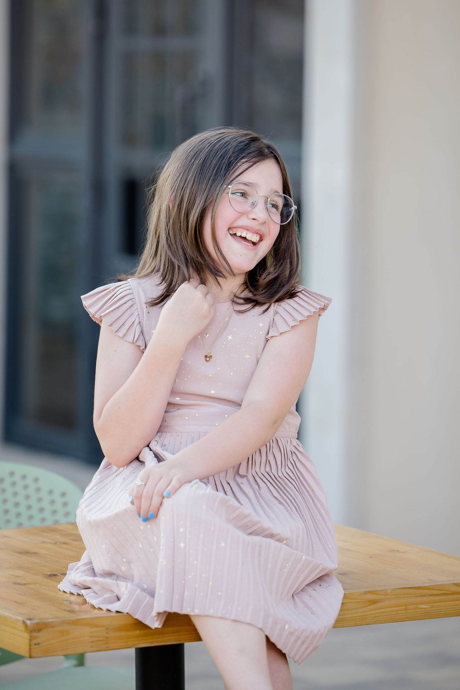A joyful portrait of someone in a pink dress sitting on a wooden bench outdoors.