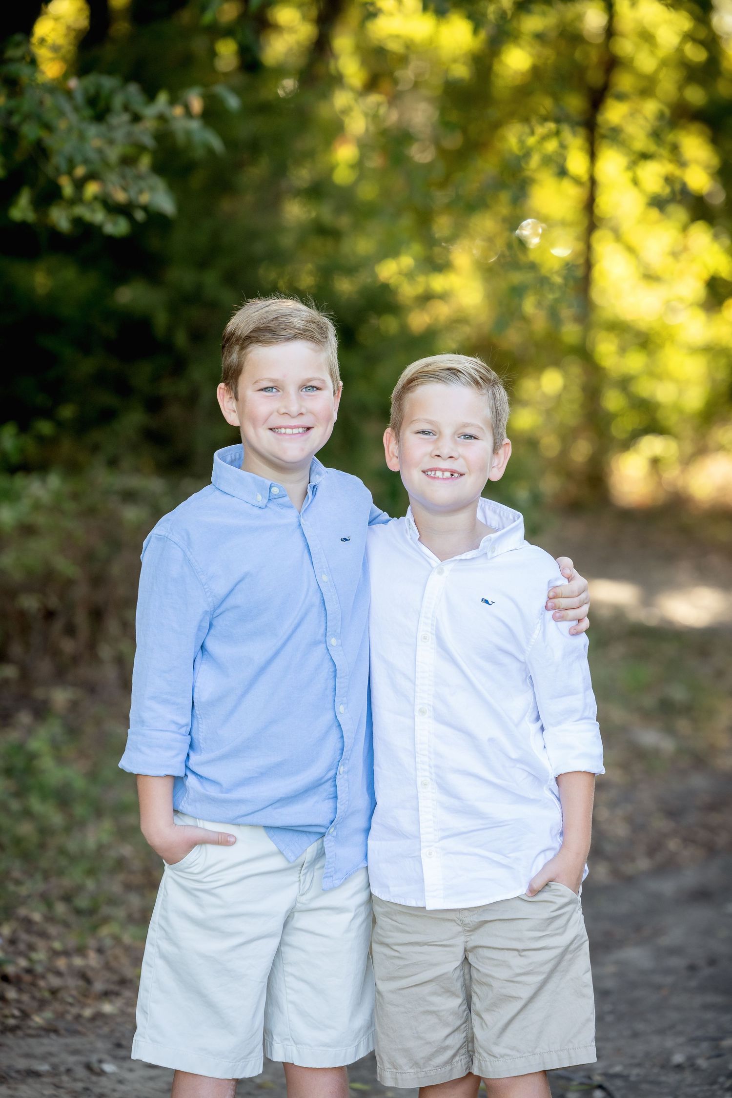 Two young people in light colored clothing pose together on a wooded path.