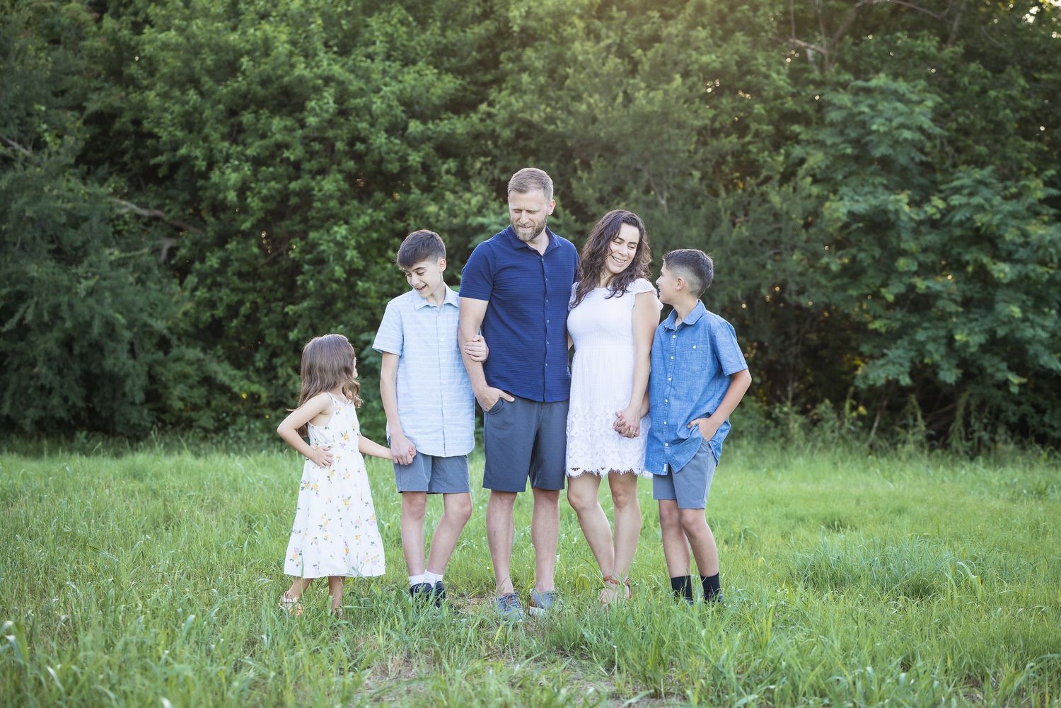 A family group poses together in casual clothing on a grassy field at sunset.