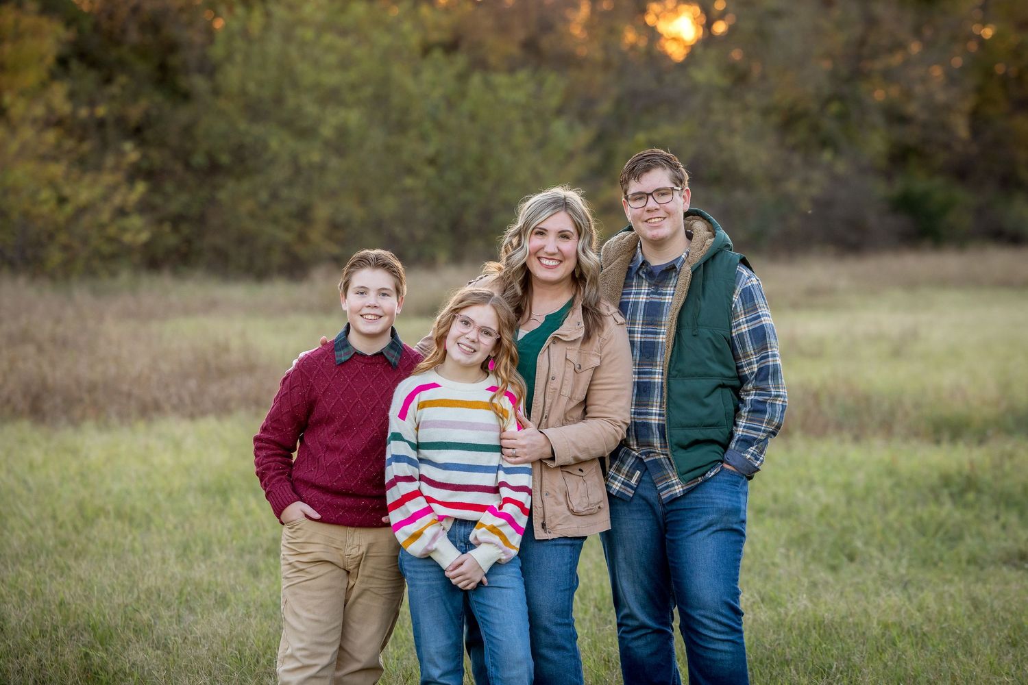 A group poses together outdoors in a grassy field at golden hour.