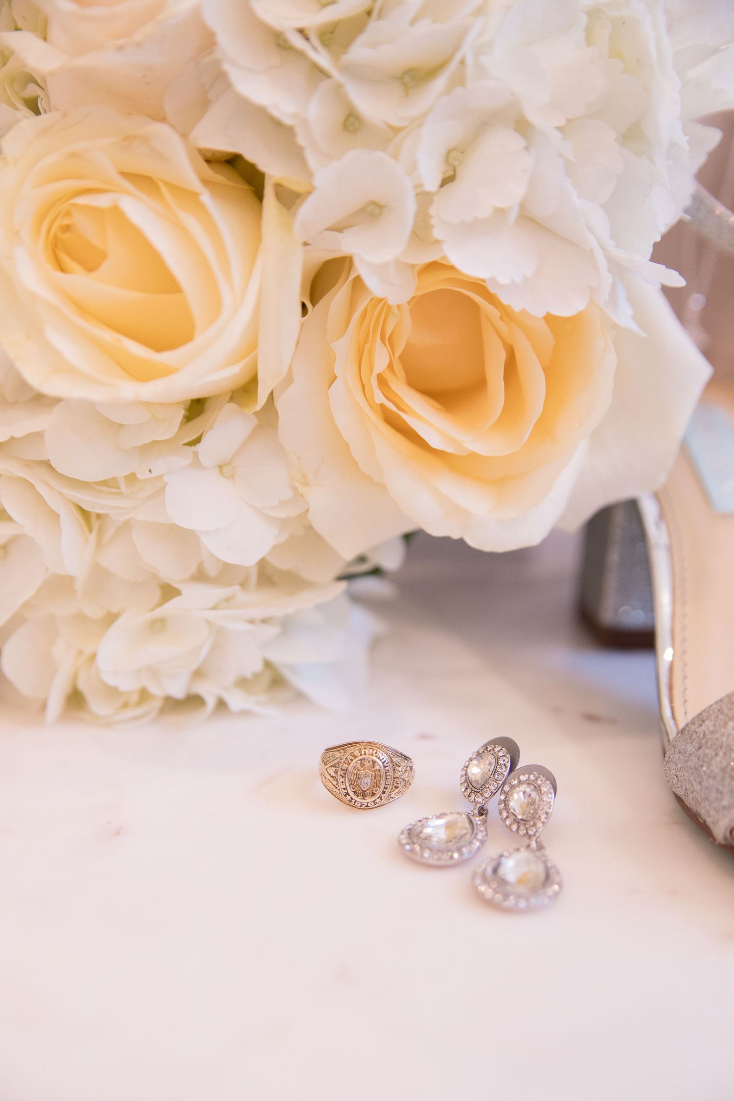 Elegant cream roses arranged next to sparkling diamond earrings and a gold ring on a white surface.