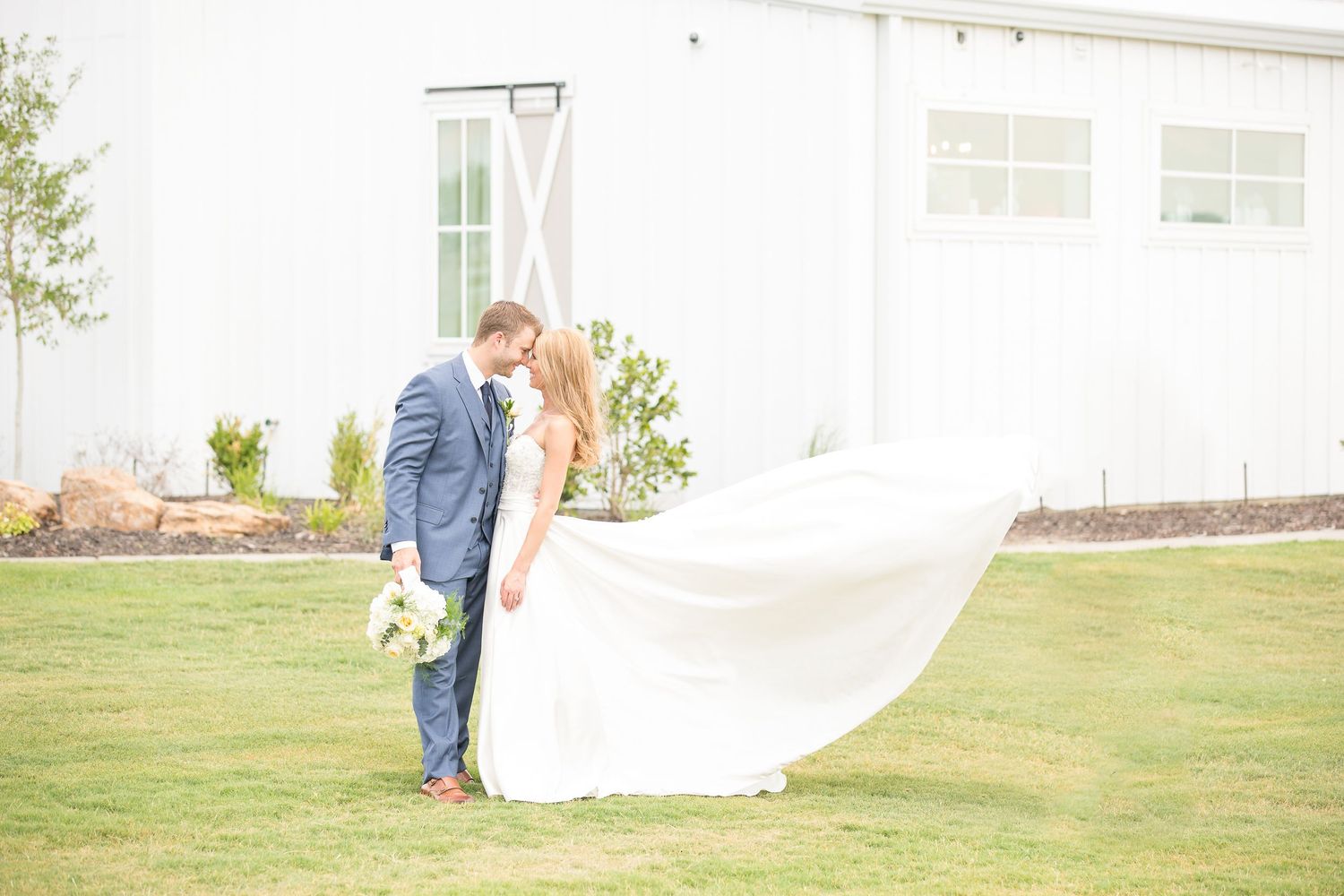 A romantic couple share a tender moment on a lush green lawn with white curtains flowing in the breeze.