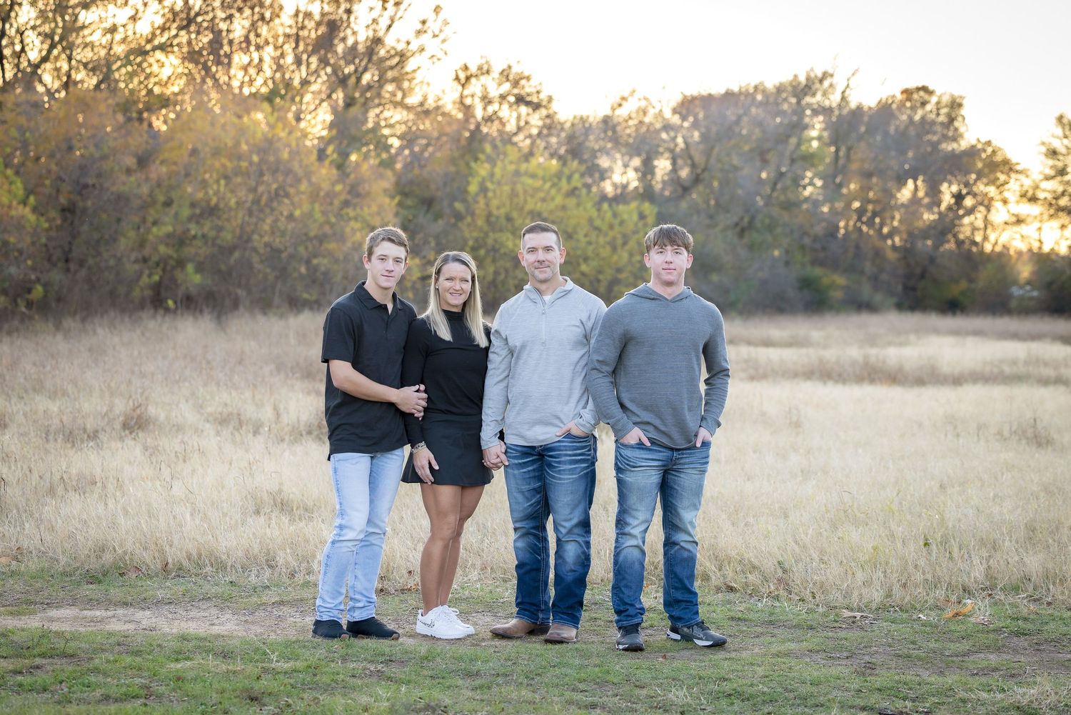 Family group poses in casual attire against natural grassland setting during sunset.