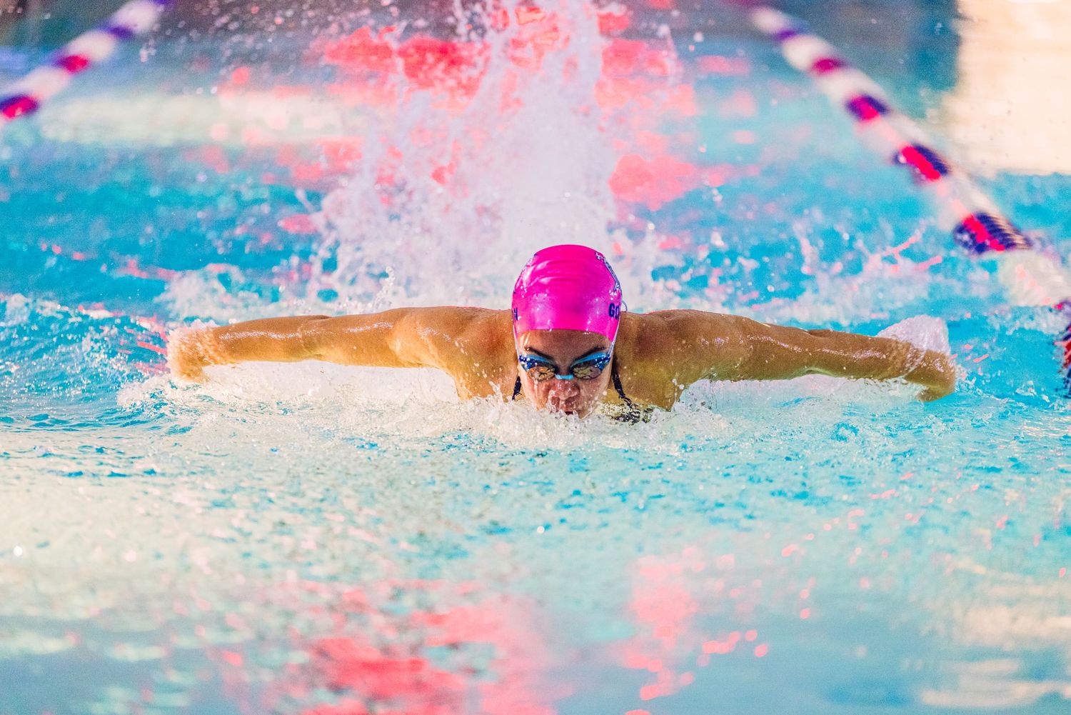 Swimmer in pink cap executing butterfly stroke in pool race with dramatic water splash.