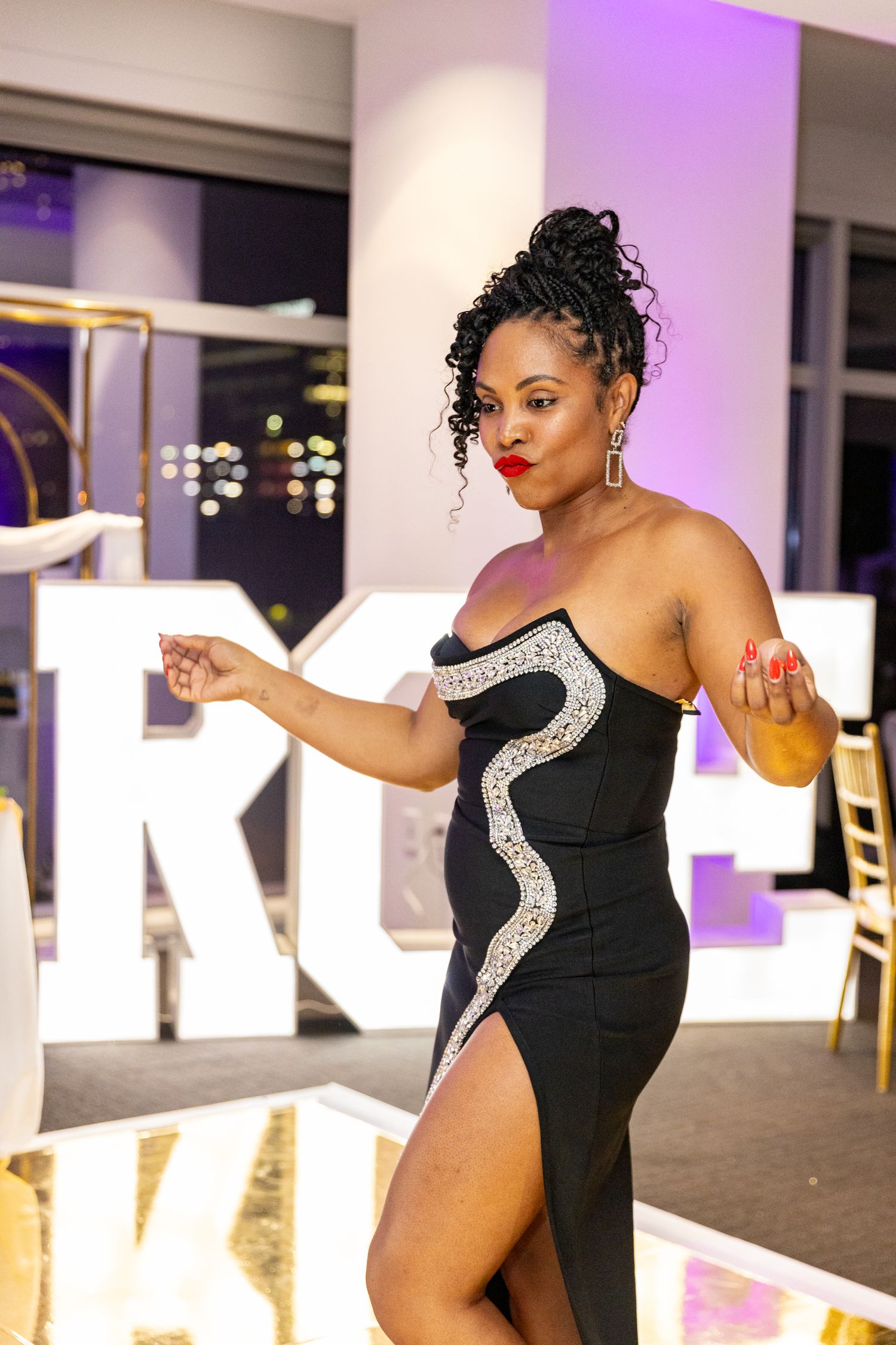 A stylish black evening gown with silver accents sparkles under purple event lighting.