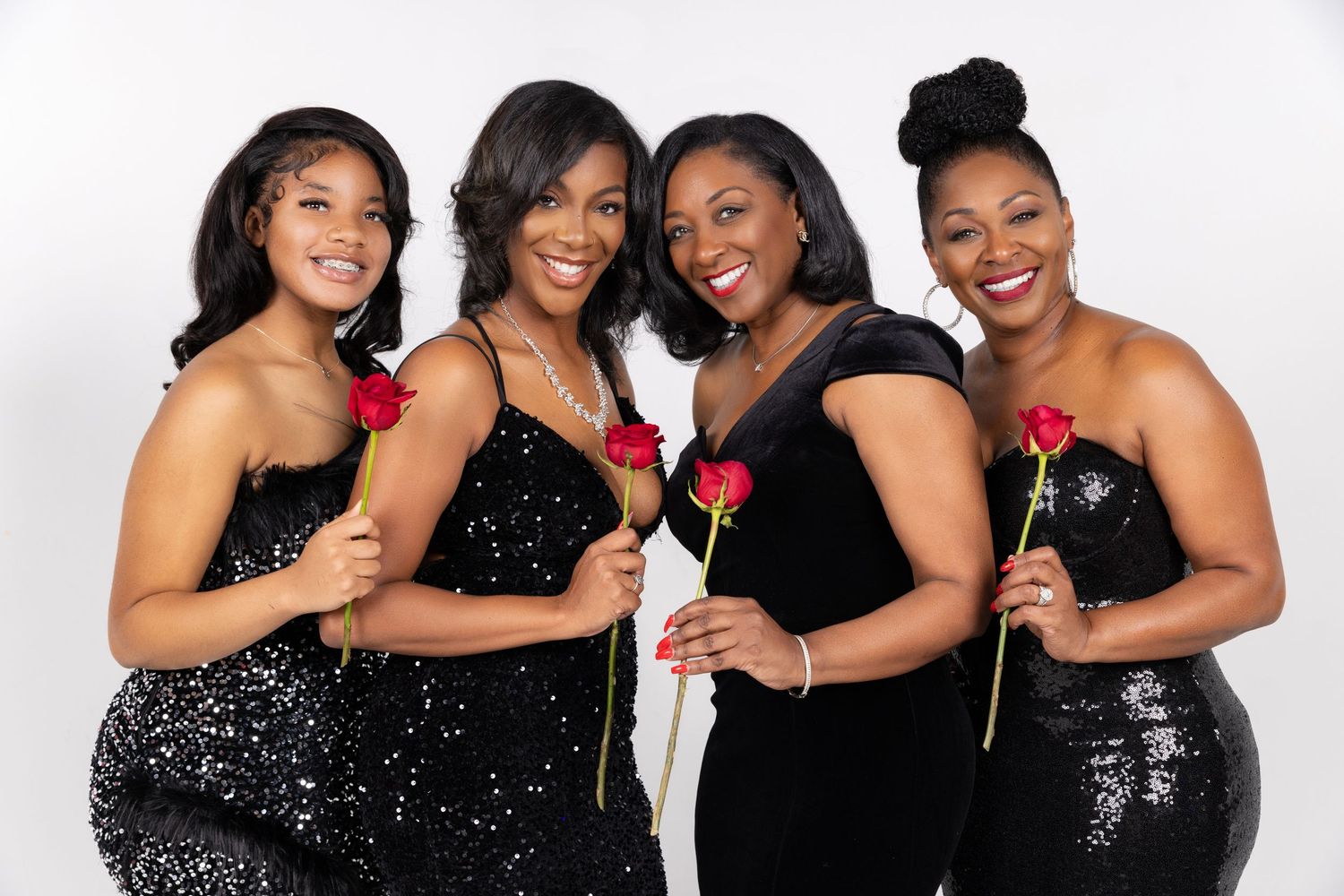 Four women in black sequin dresses pose elegantly with red roses against white background.