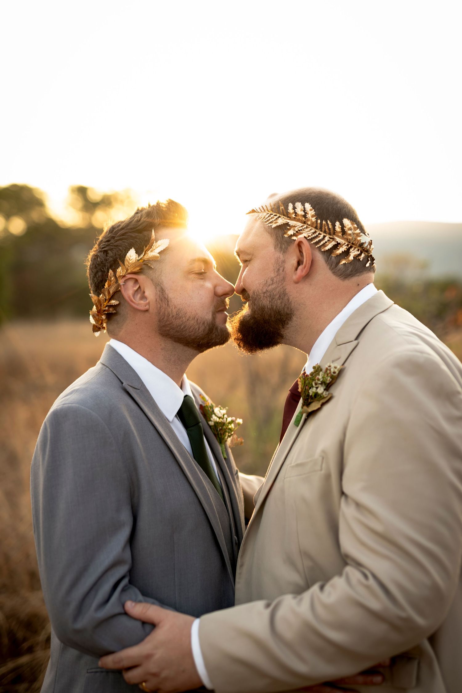 Two grooms embracing closely at sunset at their wedding