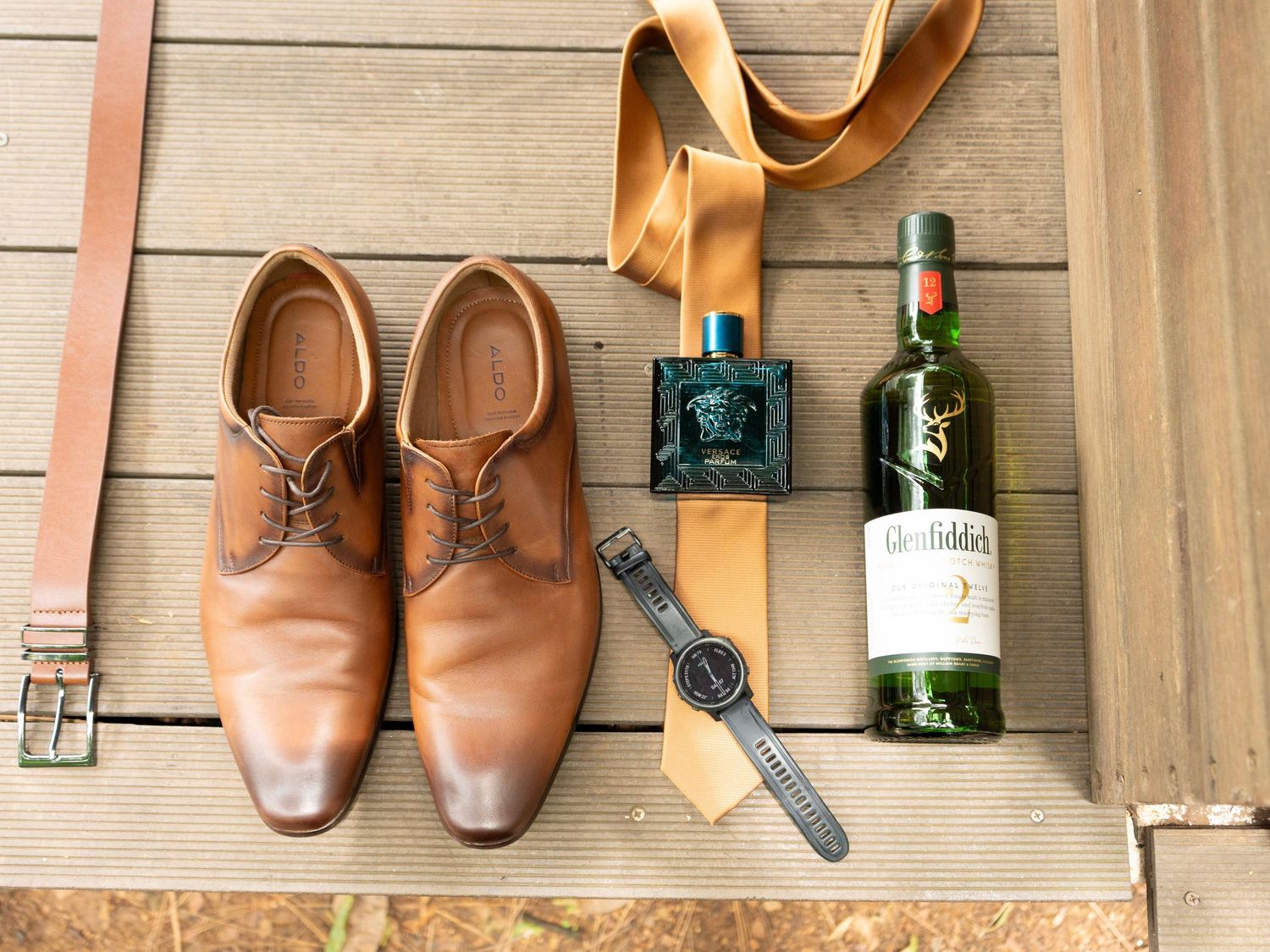Groom's accessories flat lay with shoes, belt and cologne on a wooden surface