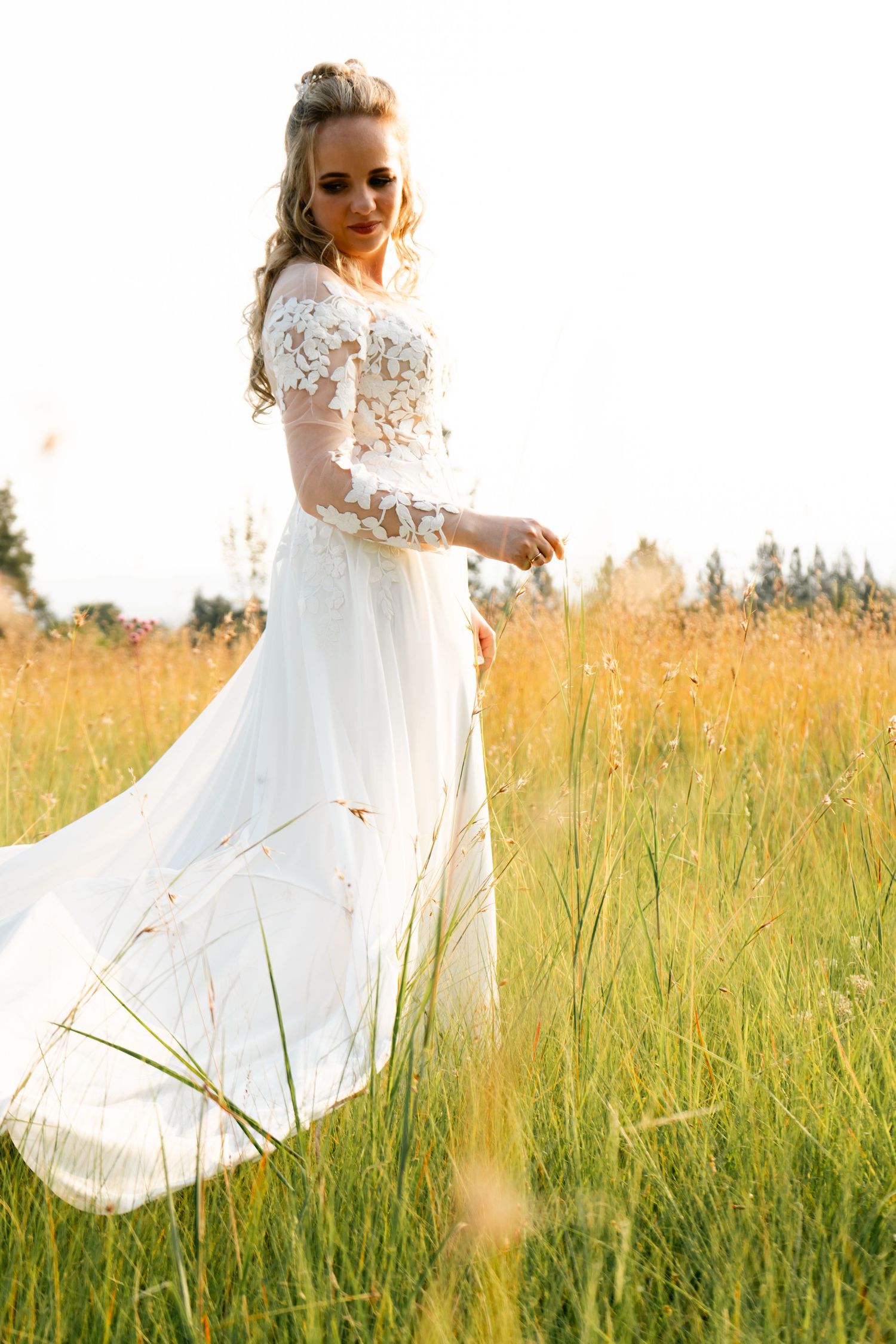 Bride in a lace wedding dress standing in a sunlit field